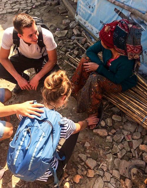 young people with backpacks praying for a rural villager