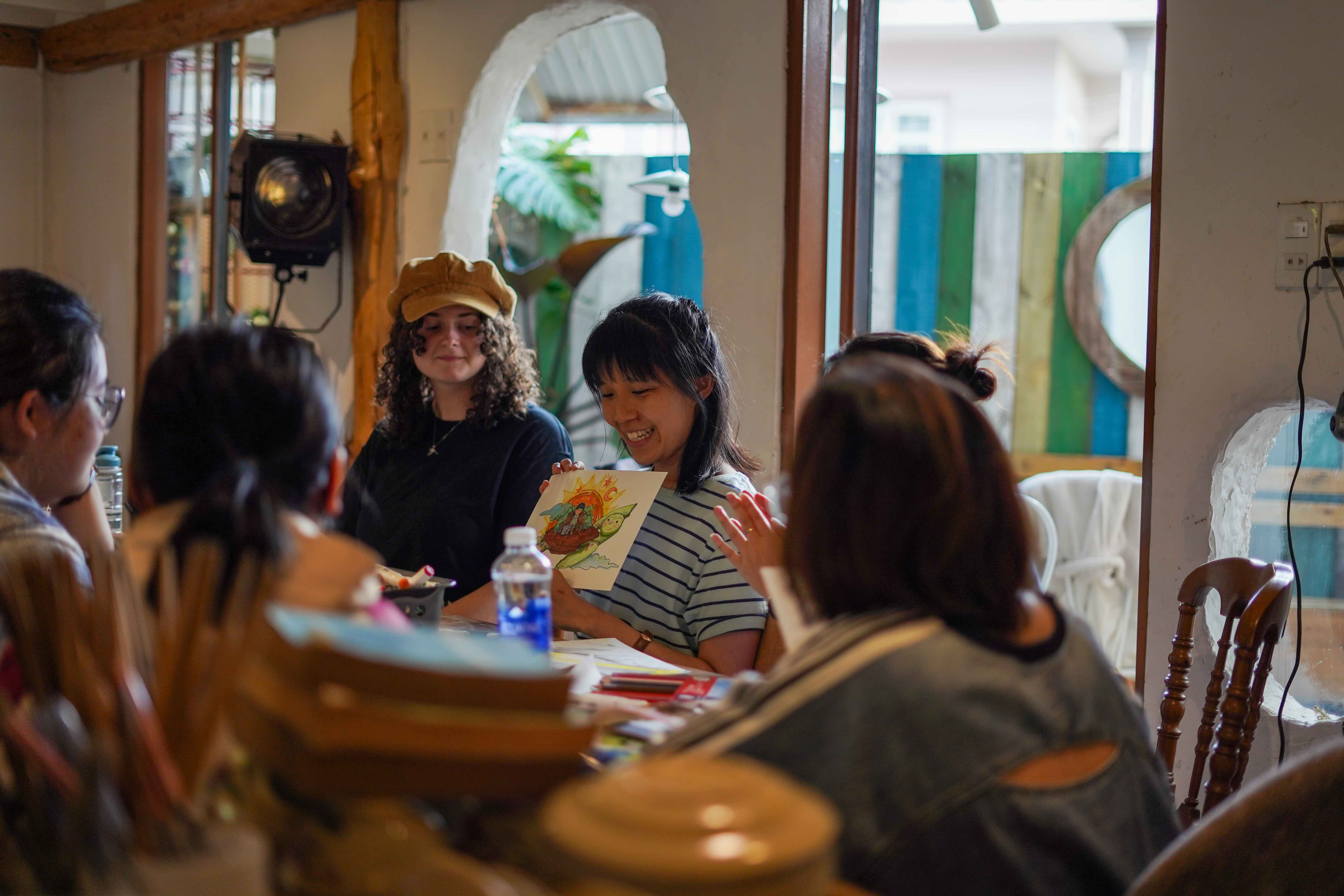 two women show a piece of art to a group 