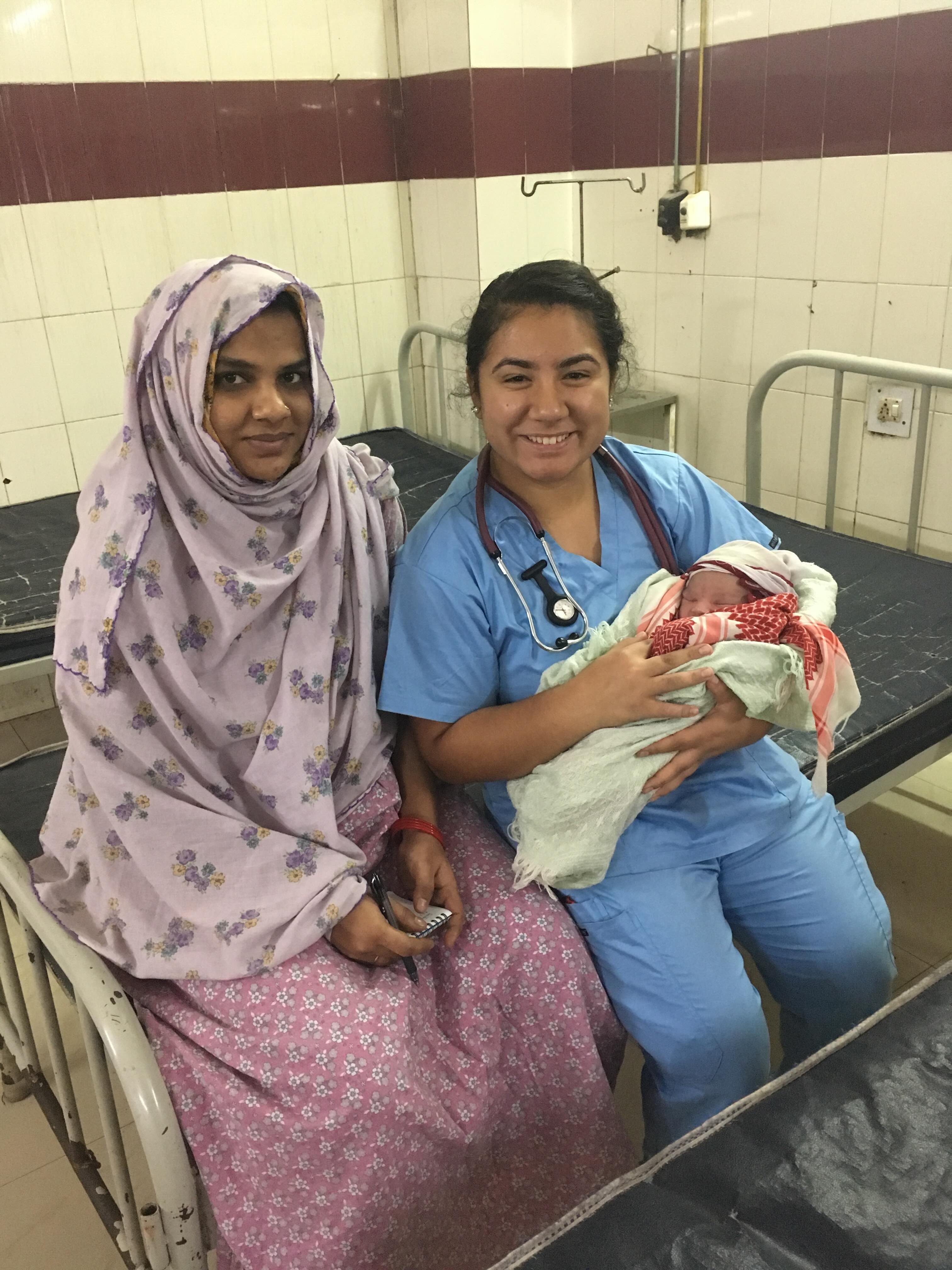a mom and a female health worker sit on a bed with a baby