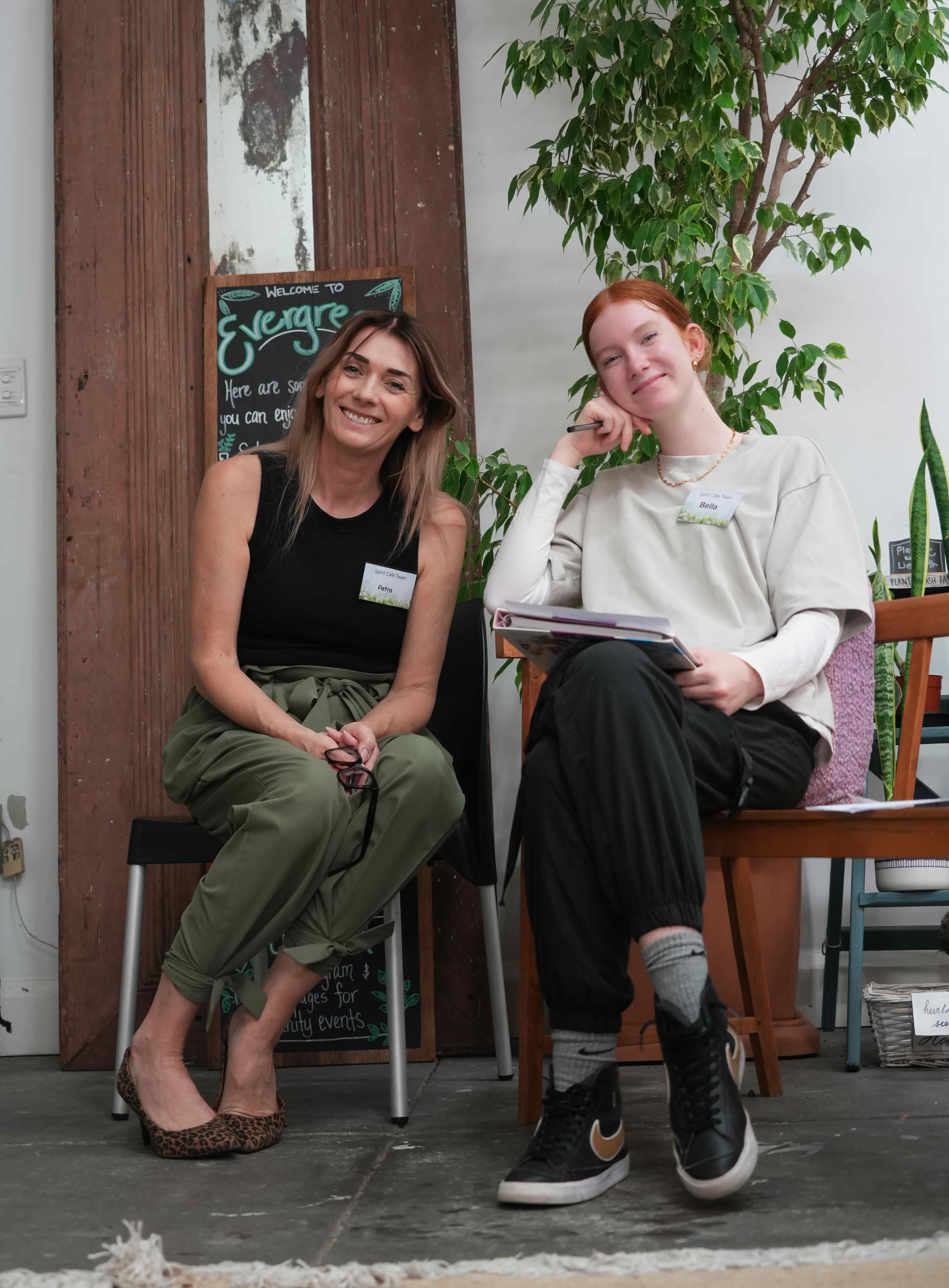 two women smile sitting in front of a shop
