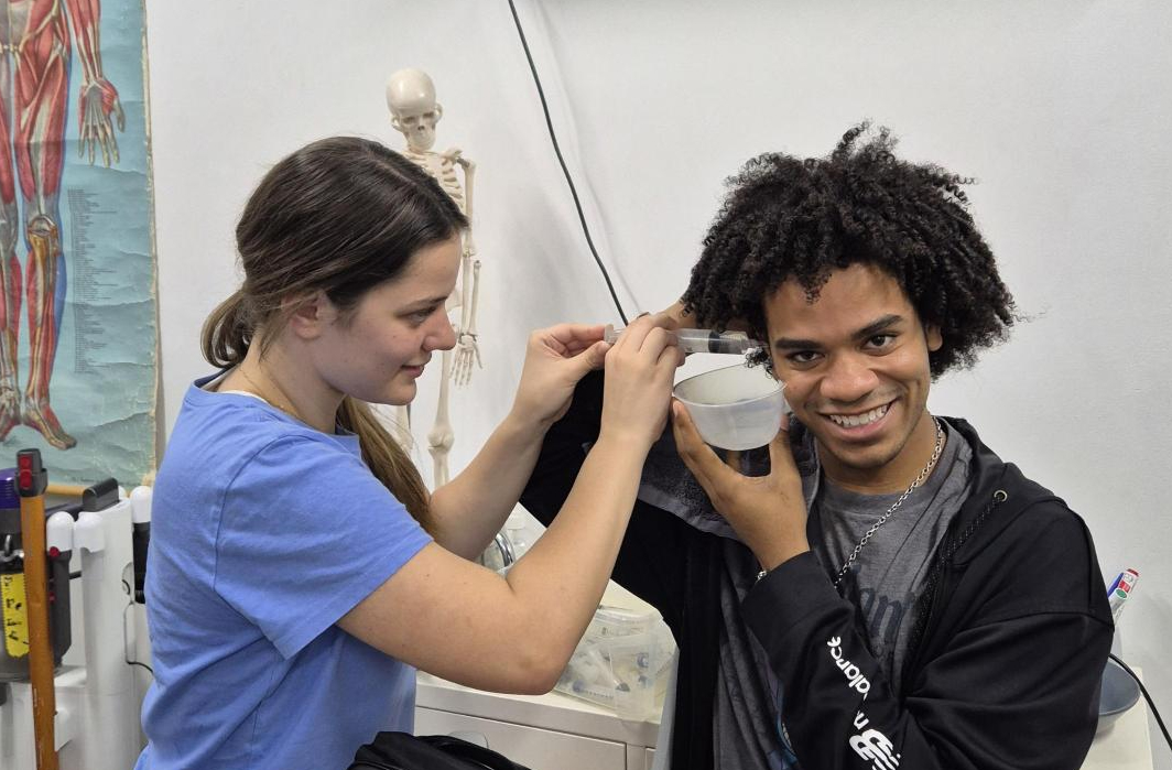 one person cleans another person's ears in a classroom