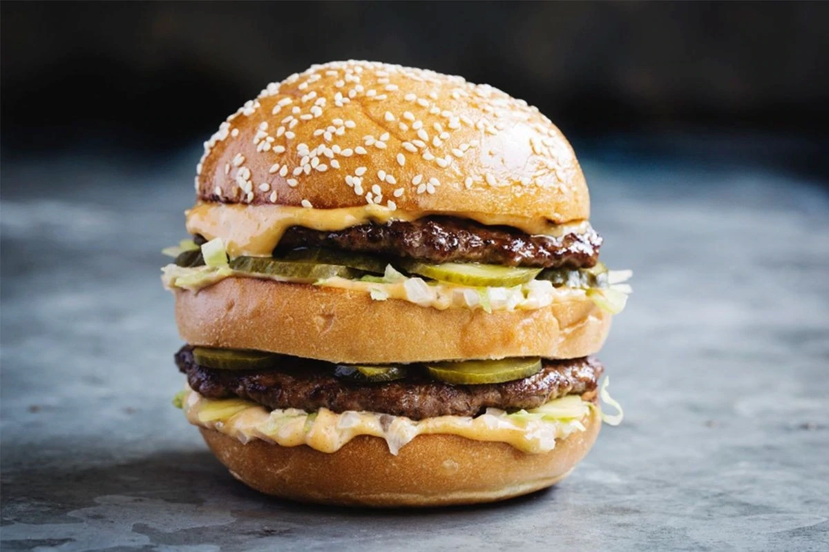 A homemade wagyu burger on a brioche bun beside a plate of lobster and caviar, illustrating the dual-service reality of a UHNW family private chef.