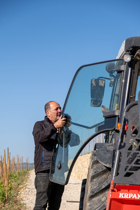 Homme ouvrant la porte vitrée d'un tracteur en plein air sous un ciel bleu clair.