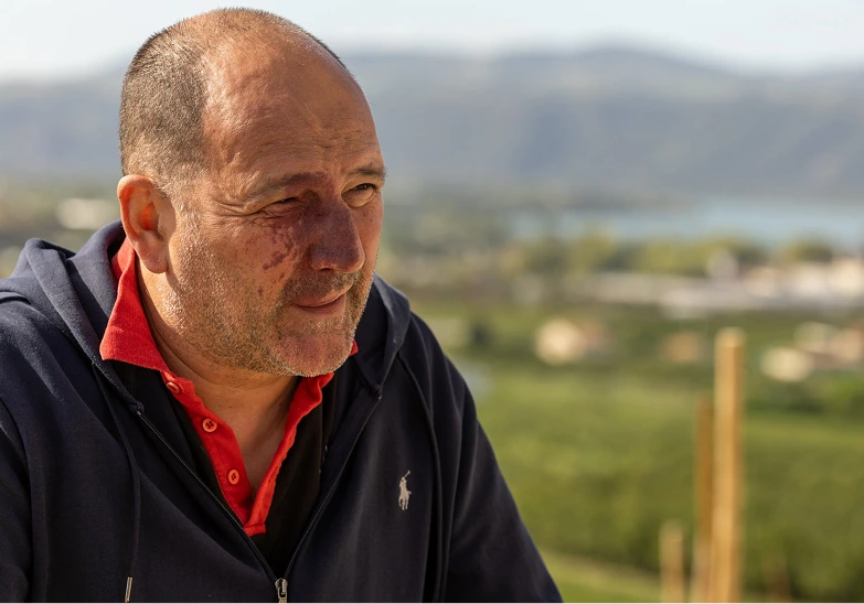 Yann Chave portant une veste noire et un polo rouge, regardant vers la droite avec un fond flou de paysage naturel.