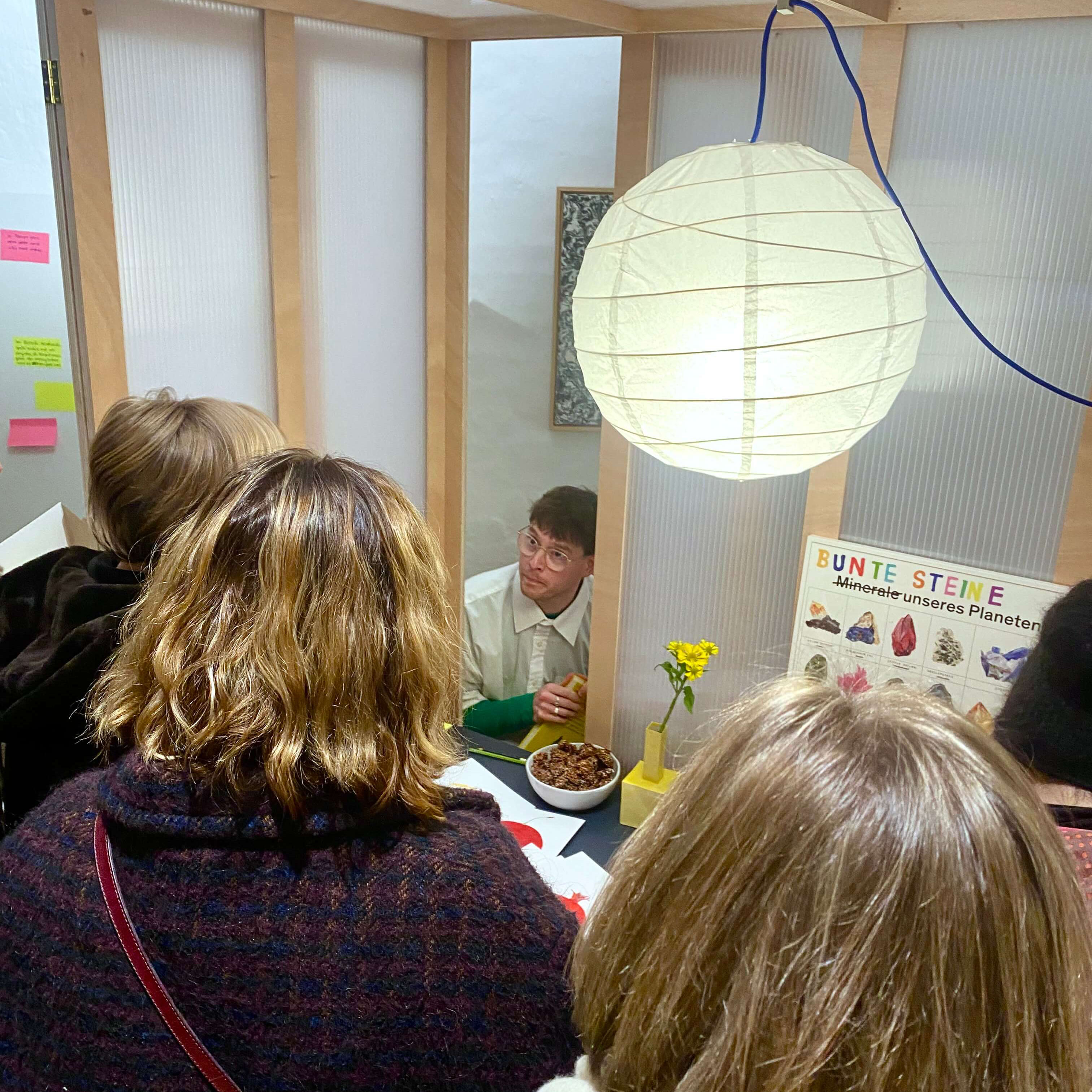 Der Künstler Felix Bork an seinem Stand im Gespräch mit Gästen. Auf dem Tisch liegen seine Bücher, an der Wand hängt ein Poster über Mineralien.