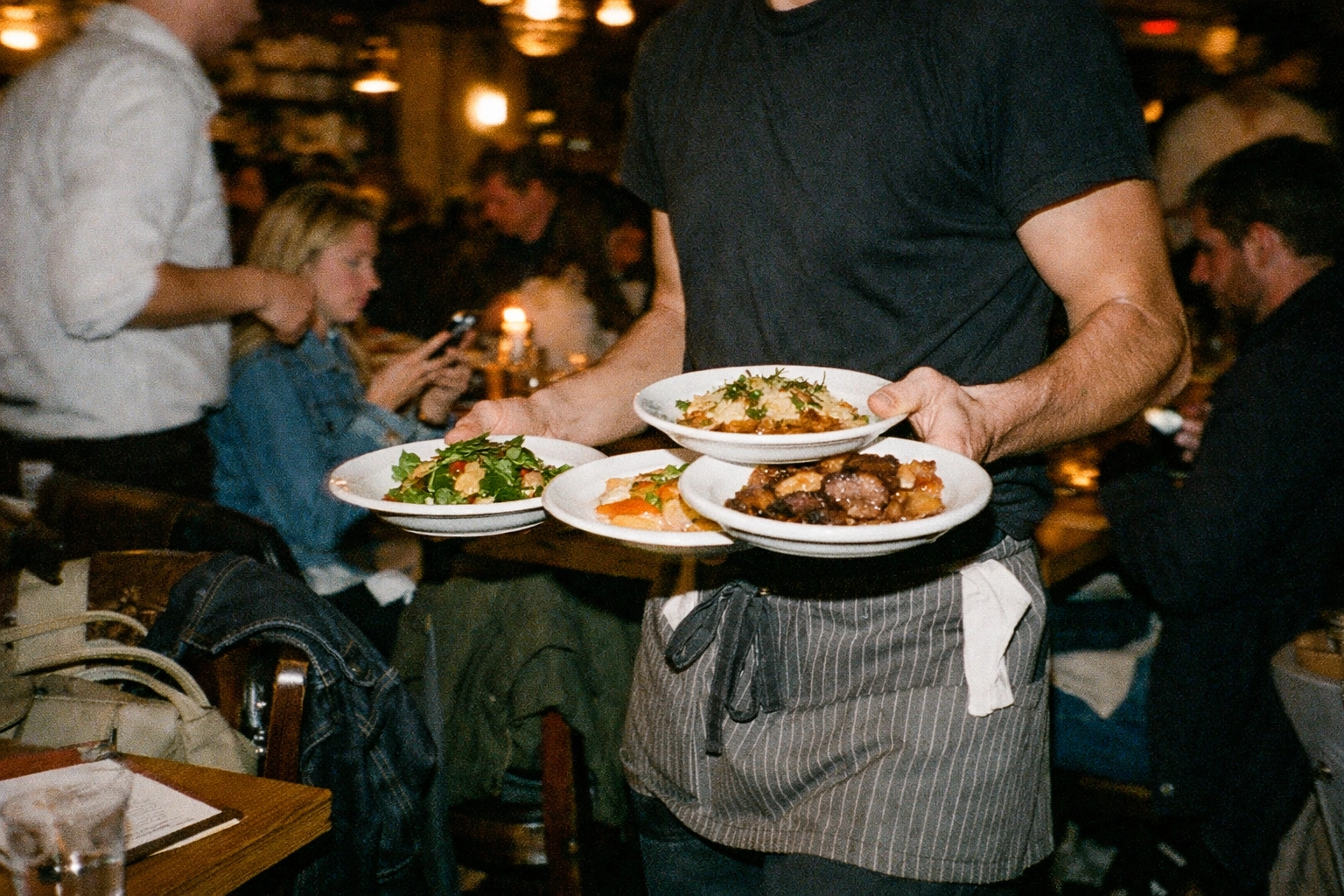 Restaurant server carrying plates during busy dinner service with diners
