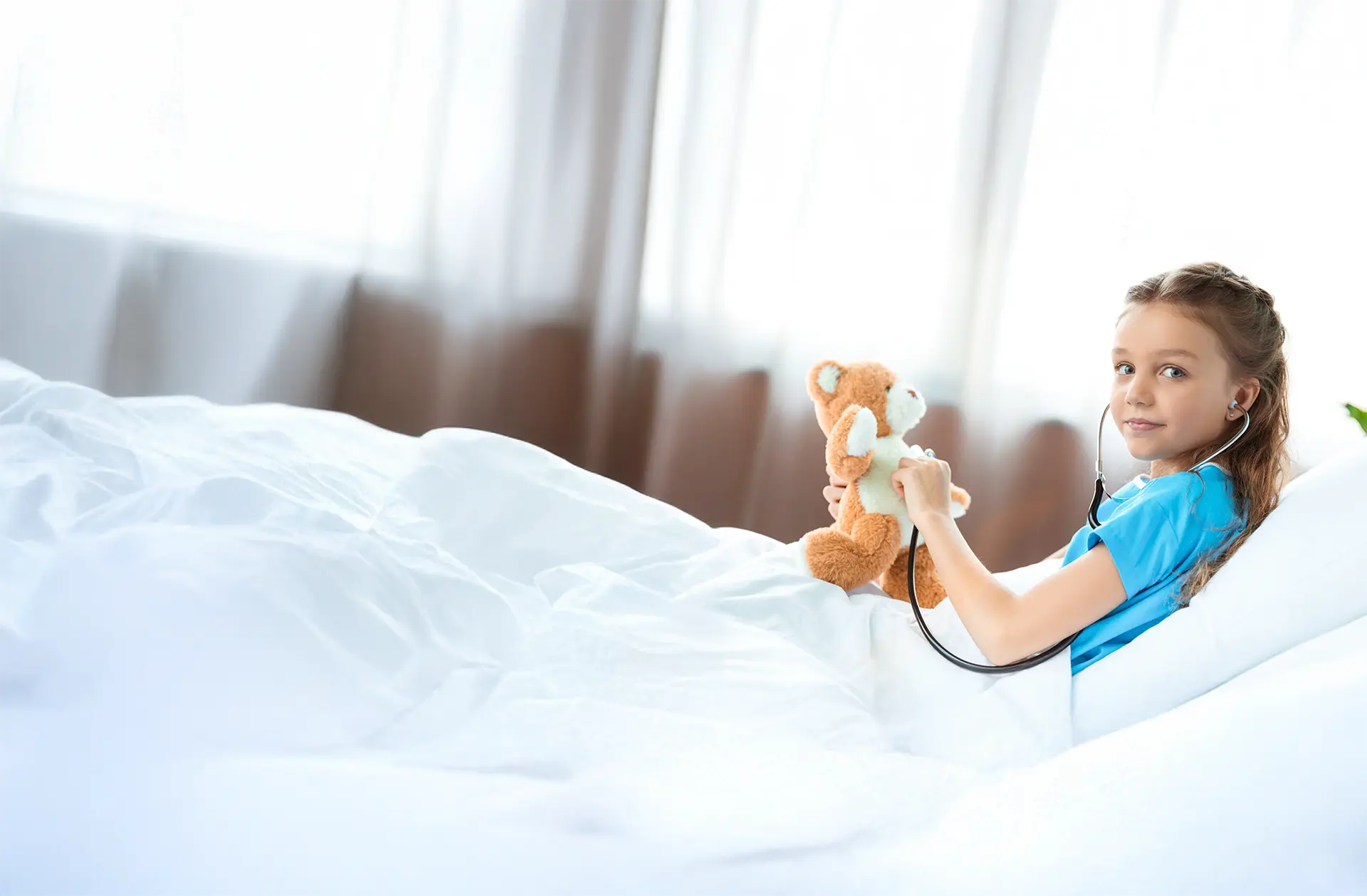 Mädchen liegt in einem Krankenhausbett und lächelt in die Kamera.