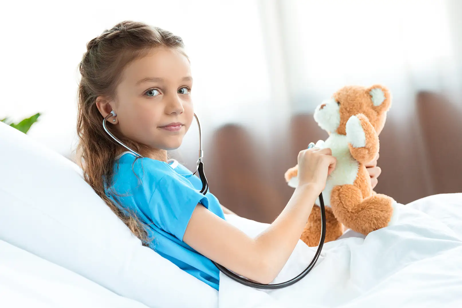 Mädchen liegt in einem Krankenhausbett und lächelt in die Kamera.