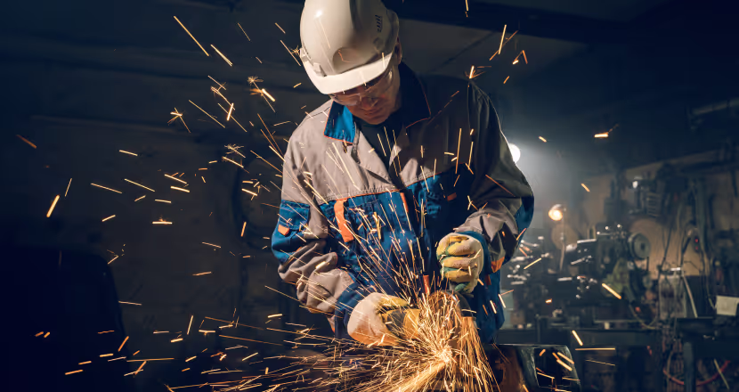 A man in an industrial setting grinds a piece of metal