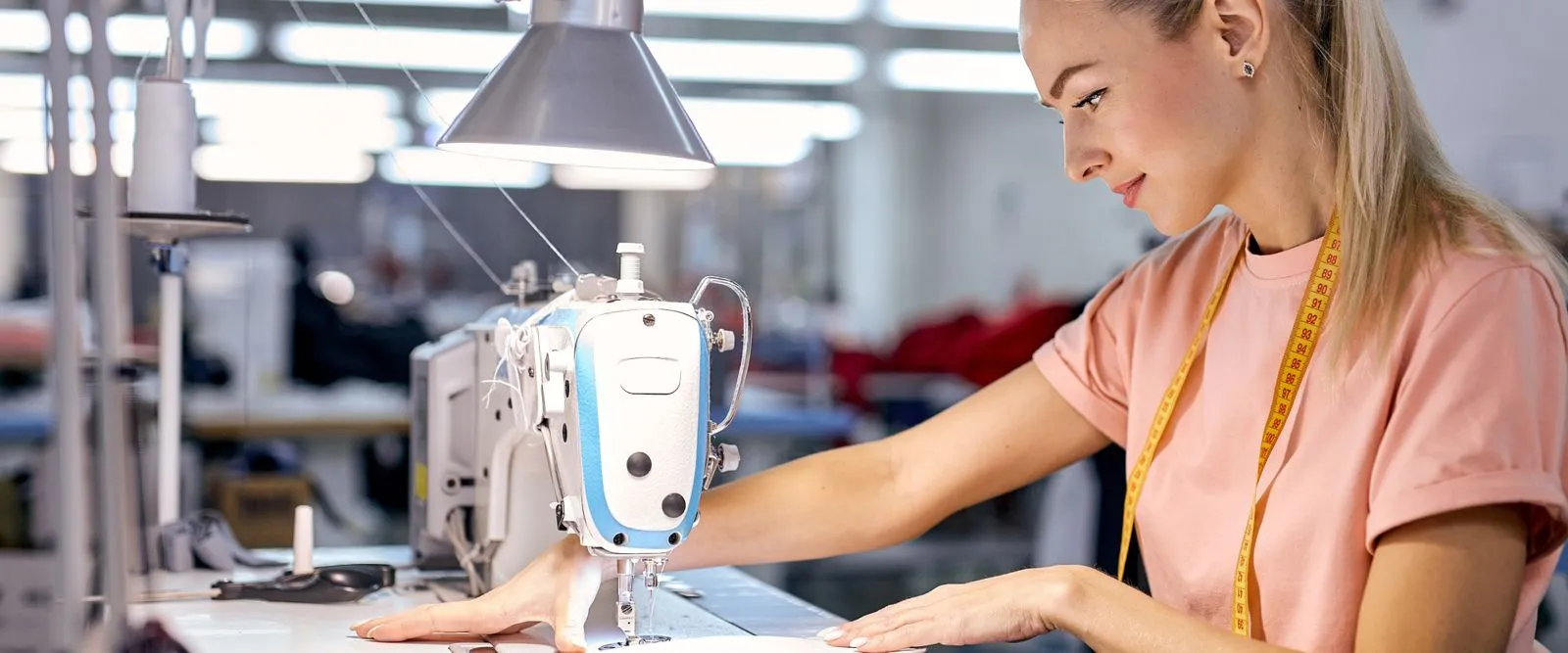 A woman sewing a garment in a large textile manufacturing facility
