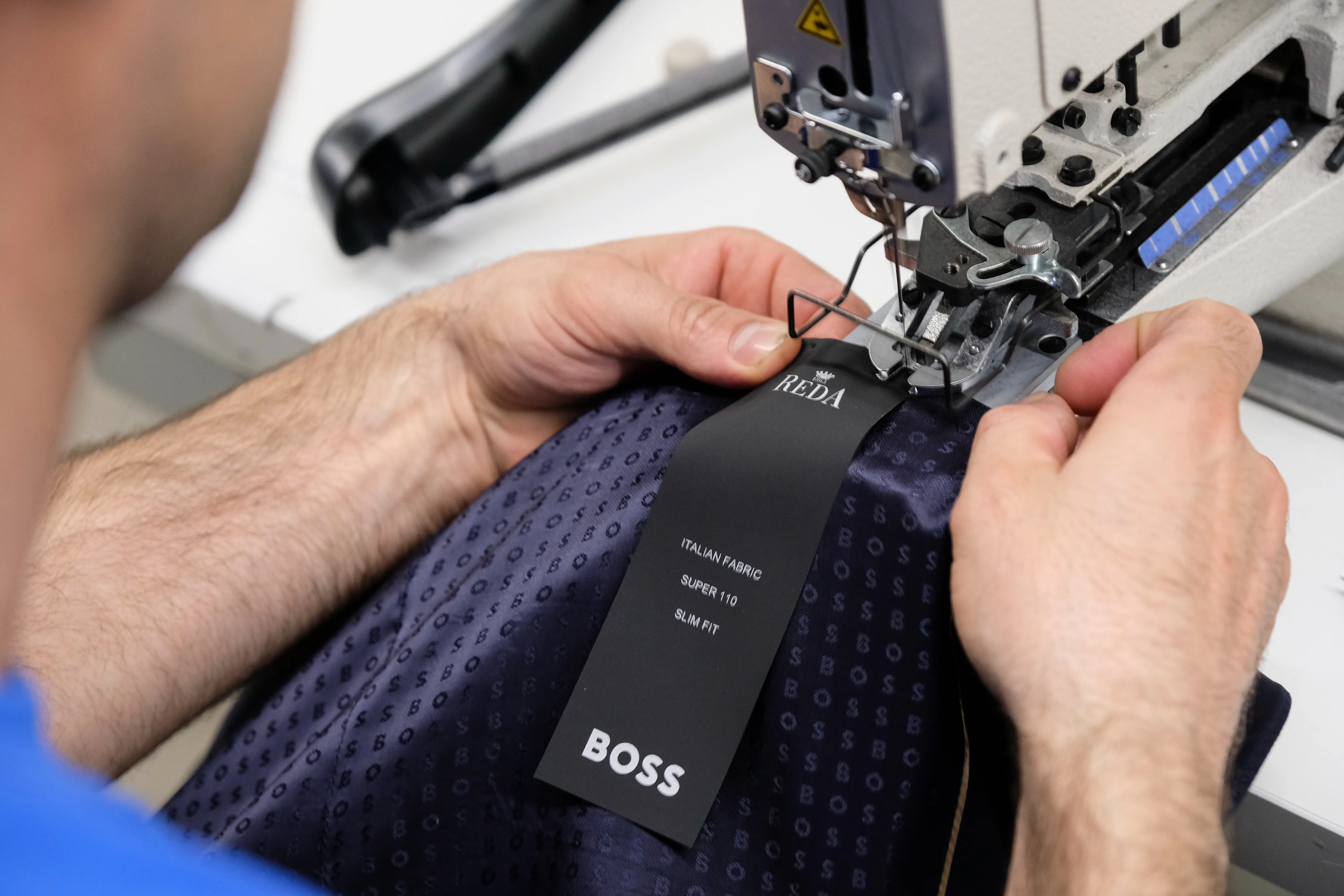 Close-up of a worker sewing a REDA and BOSS label onto a high-end garment made from Italian fabric, showcasing precision apparel manufacturing at Prevent Group.
