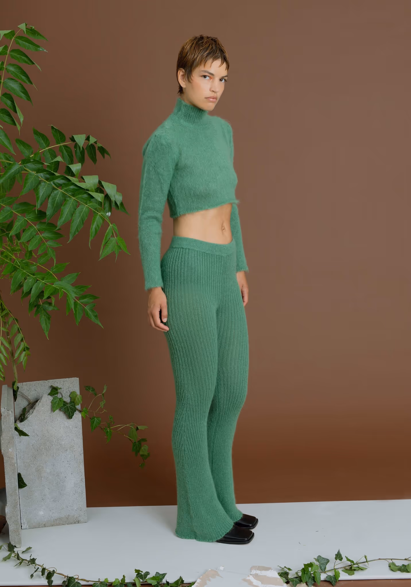 Model wearing a matching green ribbed knit set with a cropped turtleneck sweater and flared pants, showcasing contemporary loungewear produced by Prevent for emerging fashion labels.