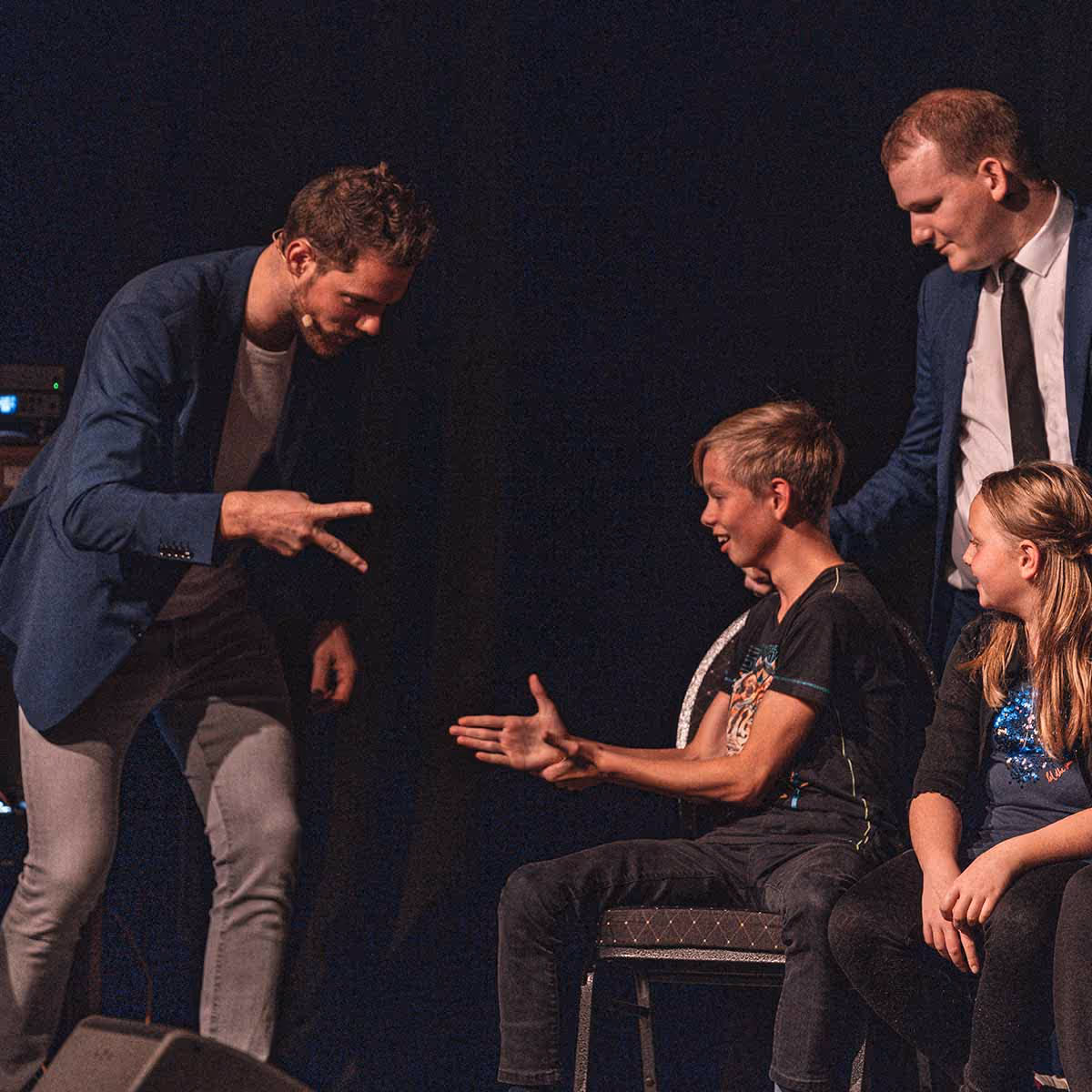 Ein Mann spielt Schere-Stein-Papier mit zwei Kindern, während ein weiterer Mann ihnen zuschaut.