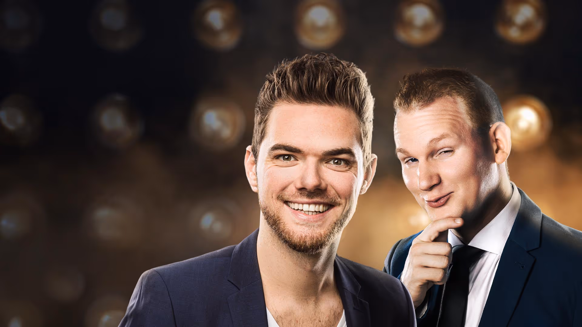 Porträt von zwei lächelnden Männern in Anzügen vor verschwommenen Lichtern.