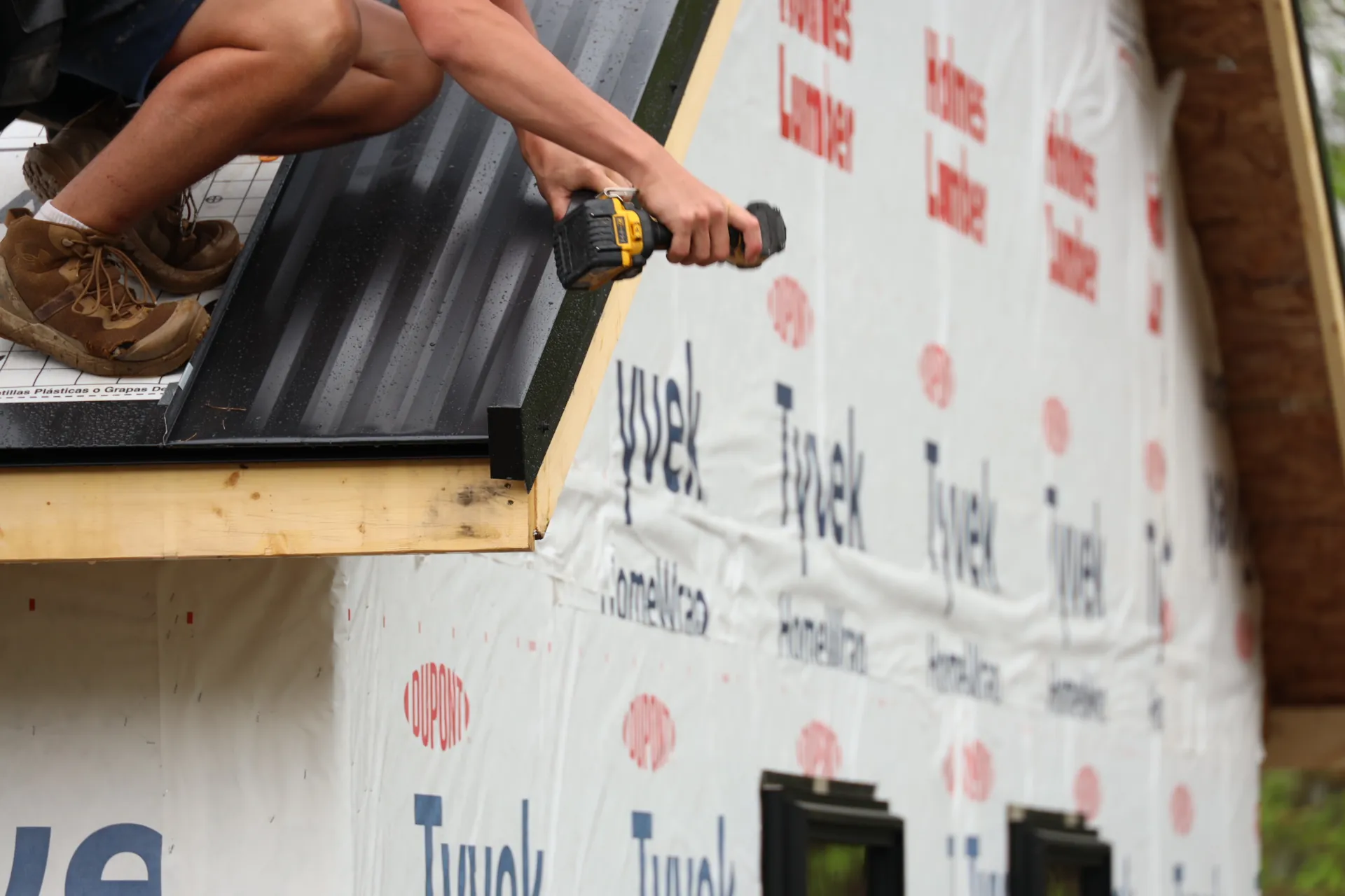 Contractor installing a metal roof panel with a drill on a residential home under construction