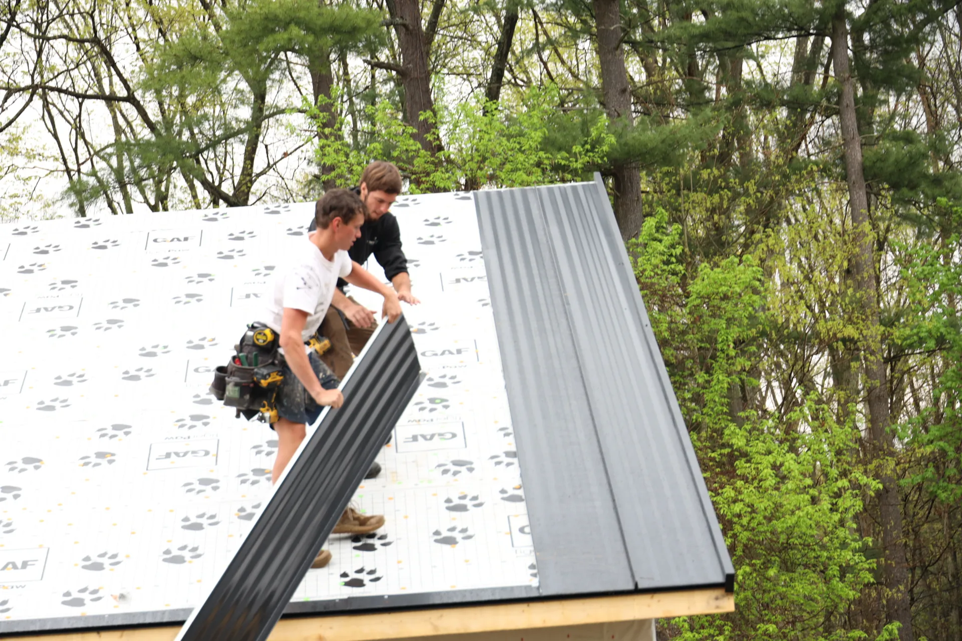 2 men installing black standing seam metal roofing on a home