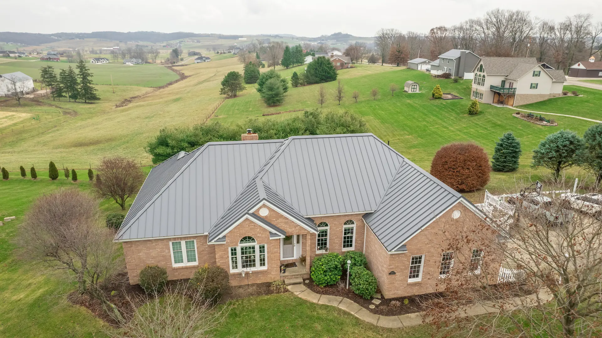 Aerial view of a brick Ohio home with a gray standing seam metal roof surrounded by a rural landscape.