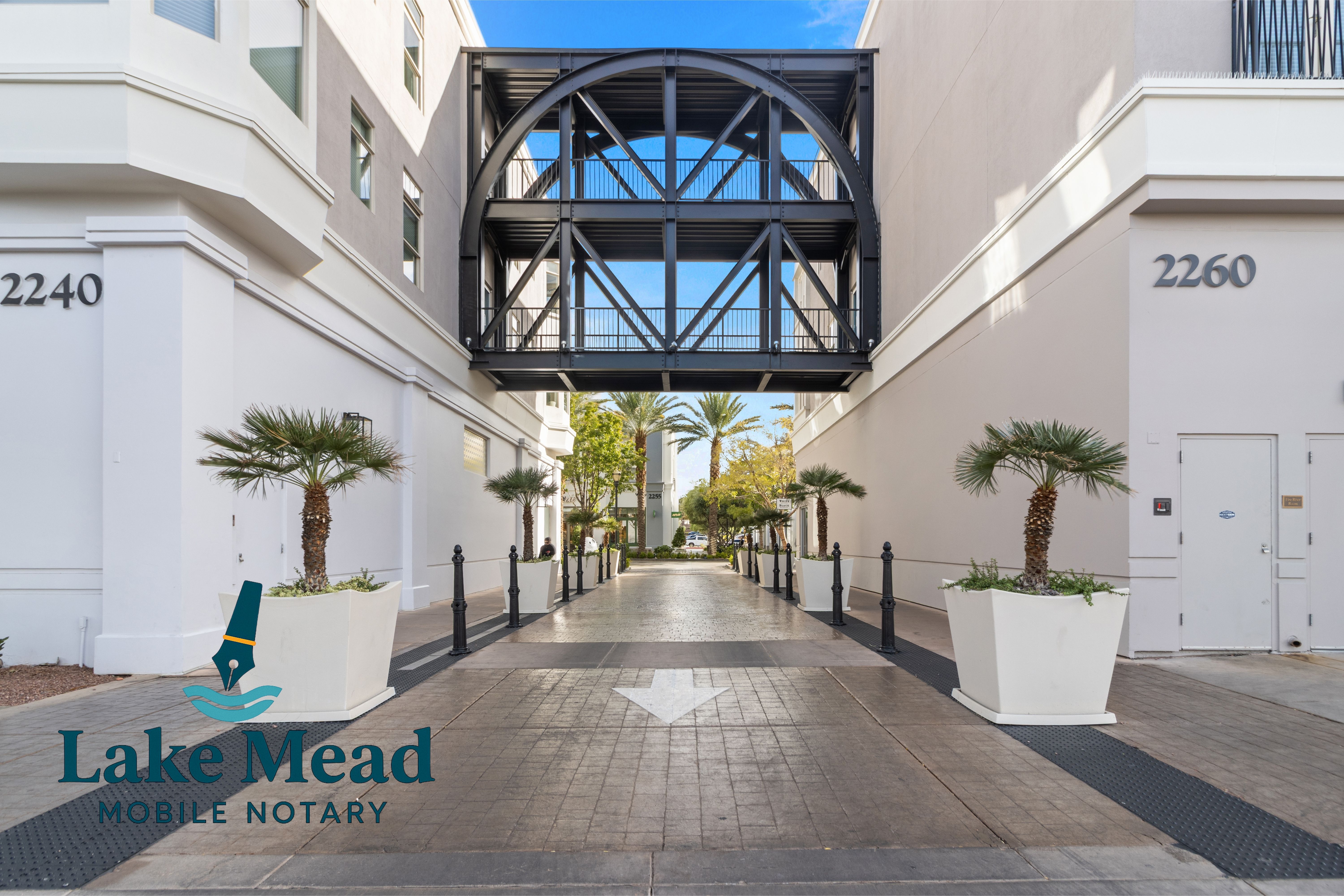 Pedestrian skybridge and walkway at The District in Henderson; planters, arrow marking, Lake Mead Mobile Notary logo visible.