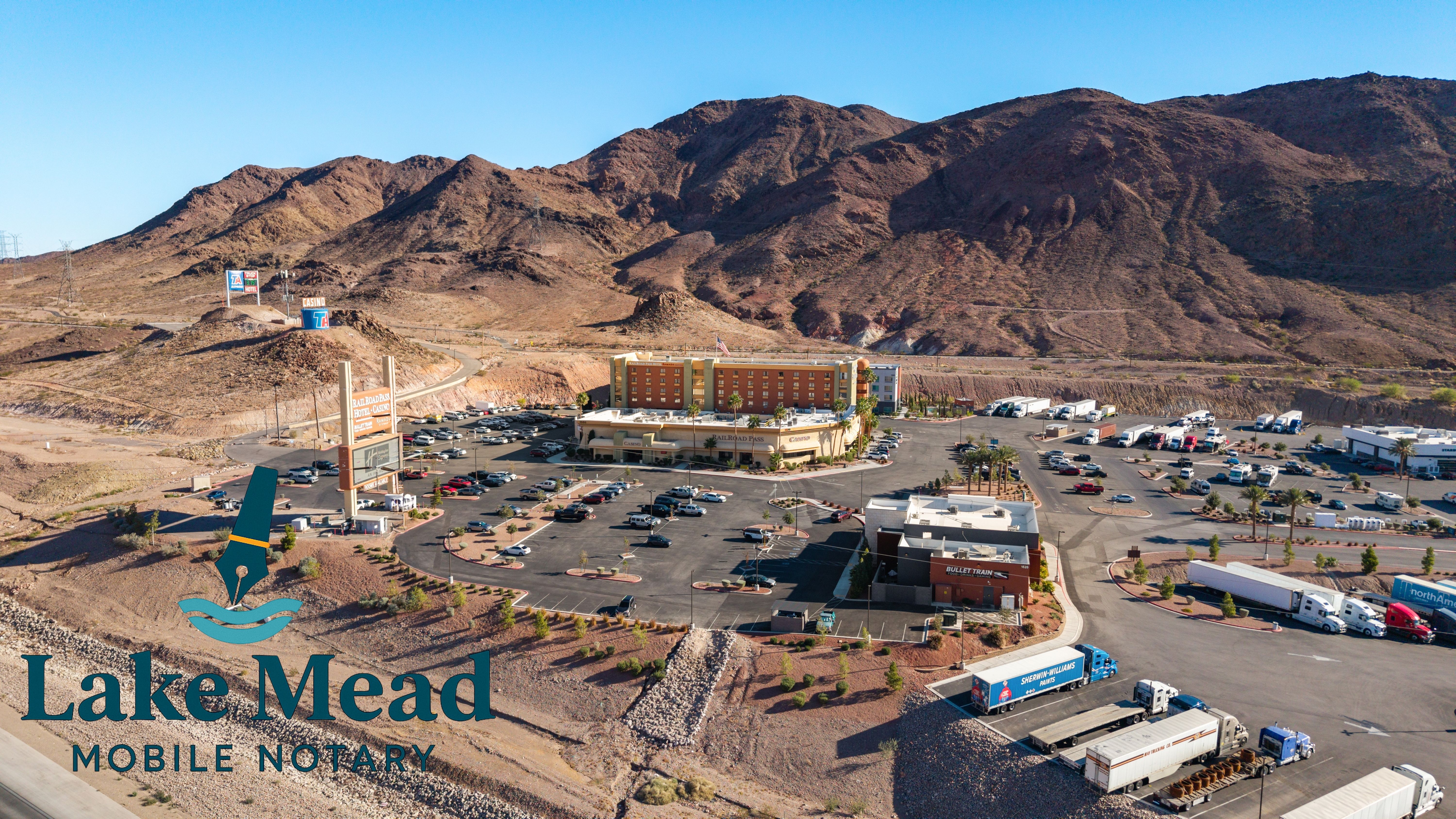 Aerial of Railroad Pass and truck plaza in Boulder City; hotel, semis parked, Lake Mead Mobile Notary logo visible.