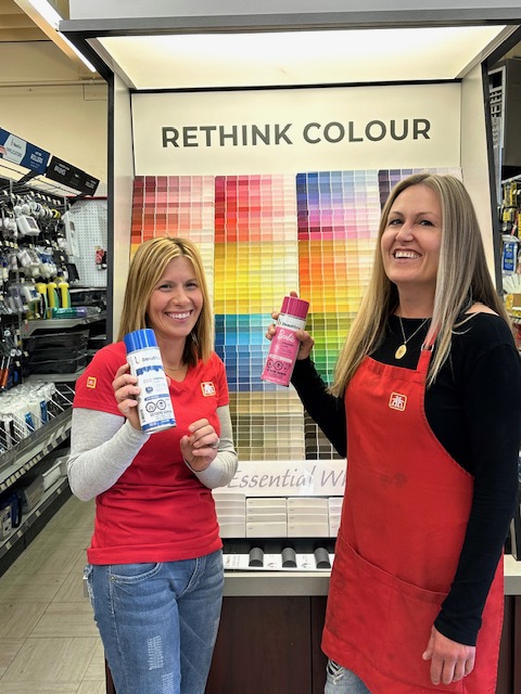 Two female Heinen Group Home Hardware employees posing in front of paint swatches