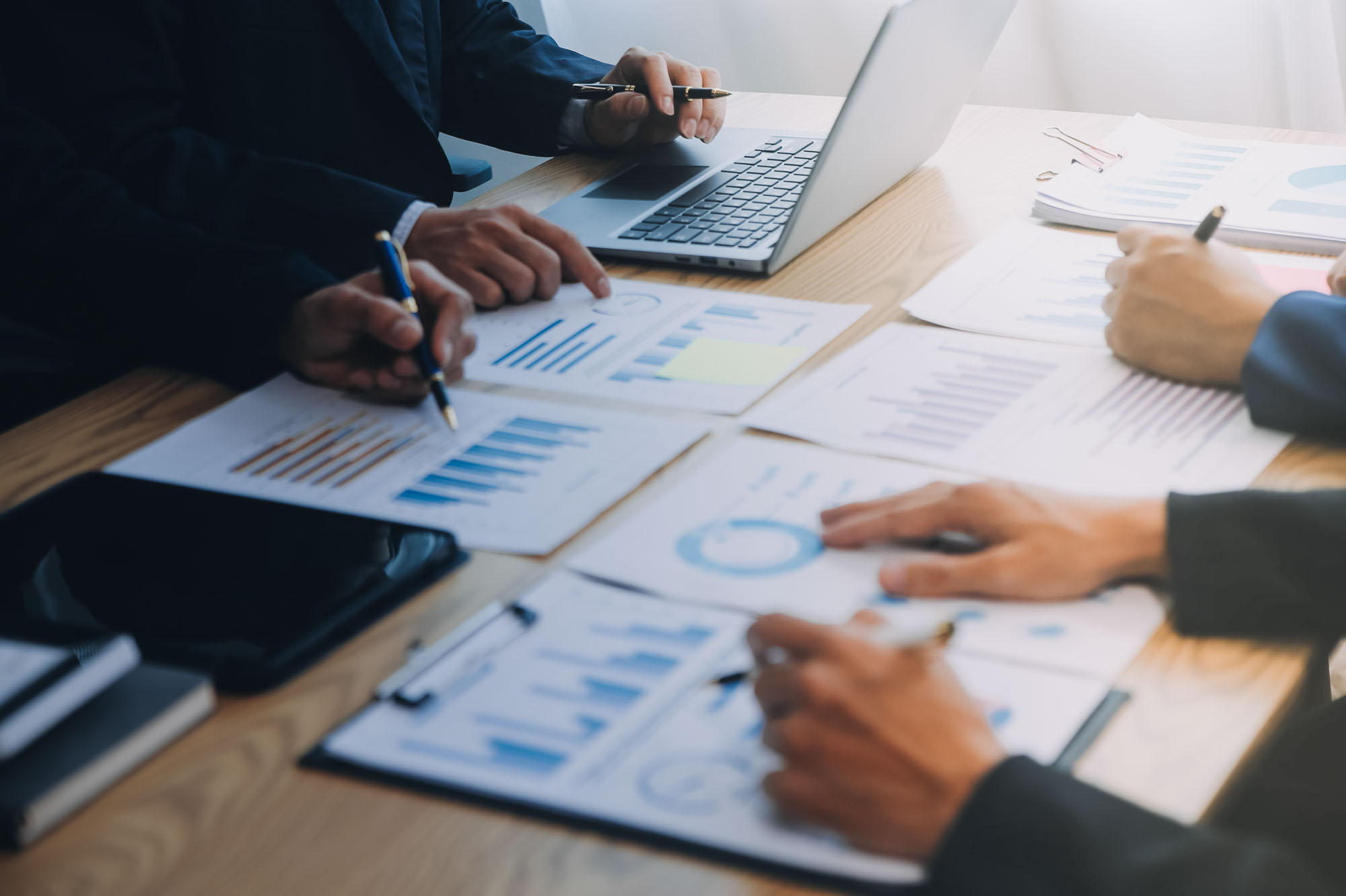 People sitting around a table reviewing graphs and charts with laptops and pens.