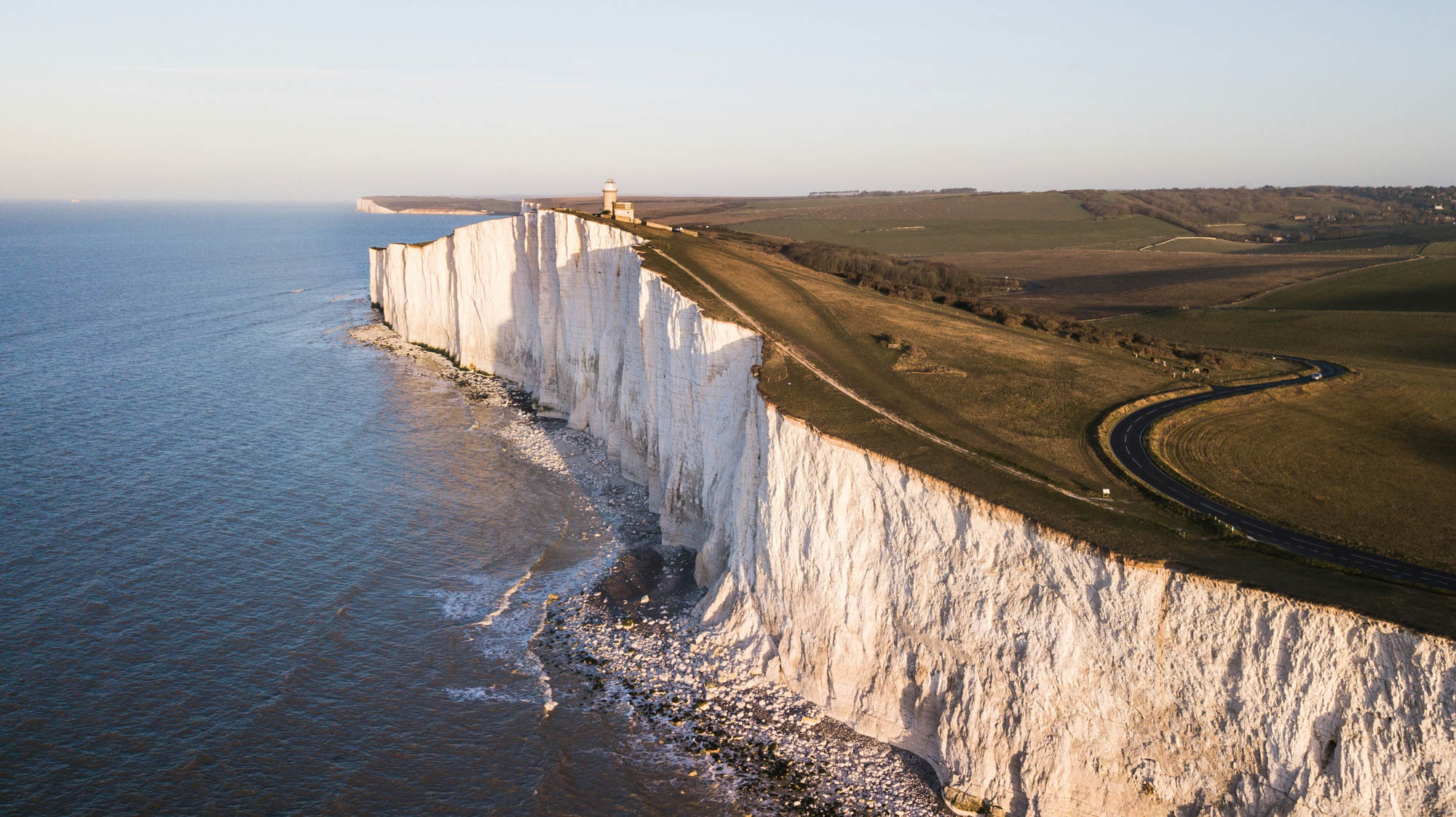 White chalk cliffs with a lighthouse on top overlooking the sea under a clear sky.