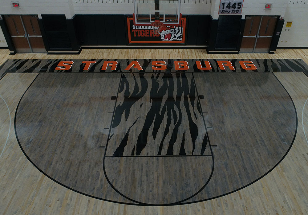 Basketball court with tiger stripe center design and Strasburg name in large orange letters.