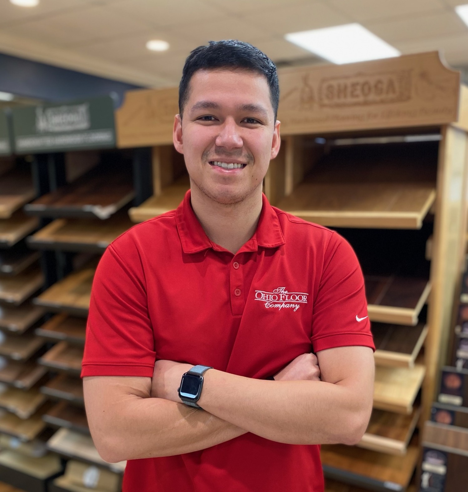 Sports Floor Salesman, wearing a red shirt with The Ohio Floor Company logo on the front standing with arms crossed in front of wooden flooring displays.