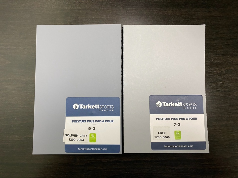 Two Tarkett Sports Polyturf Plus Pad & Pour samples labeled Dolphin Grey and Grey on a dark wood surface.