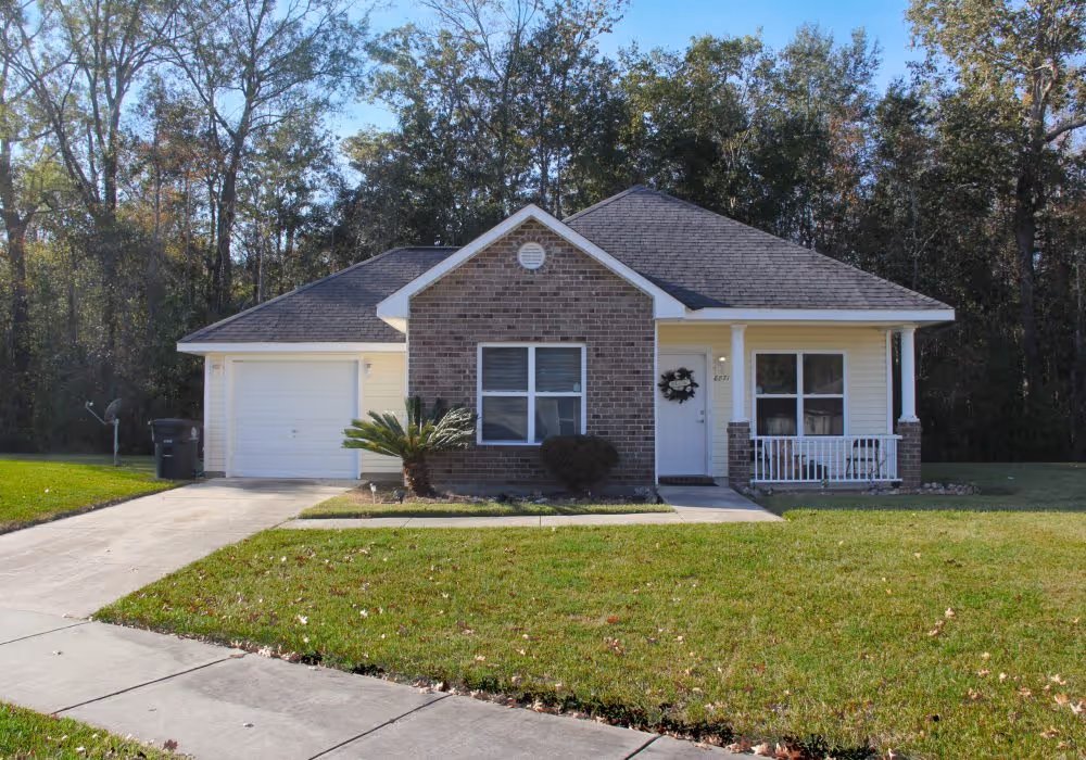 A cozy single-family home with a brick façade, one-car garage, and front porch, surrounded by peaceful wooded views.