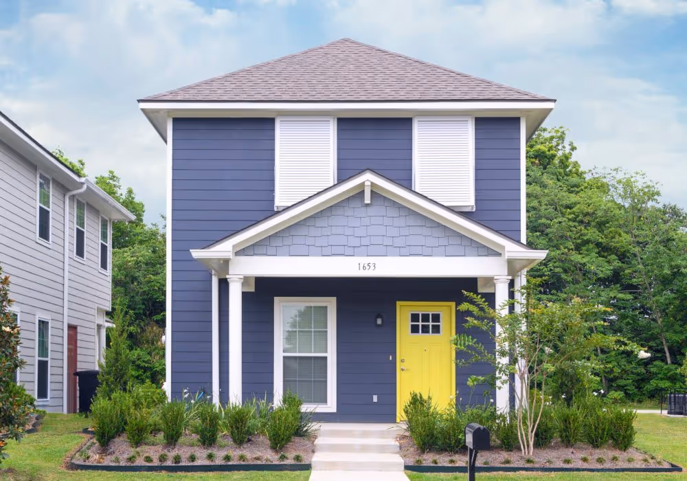 Modern two-story navy blue house with white trim, a bright yellow front door, and neatly landscaped yard.
