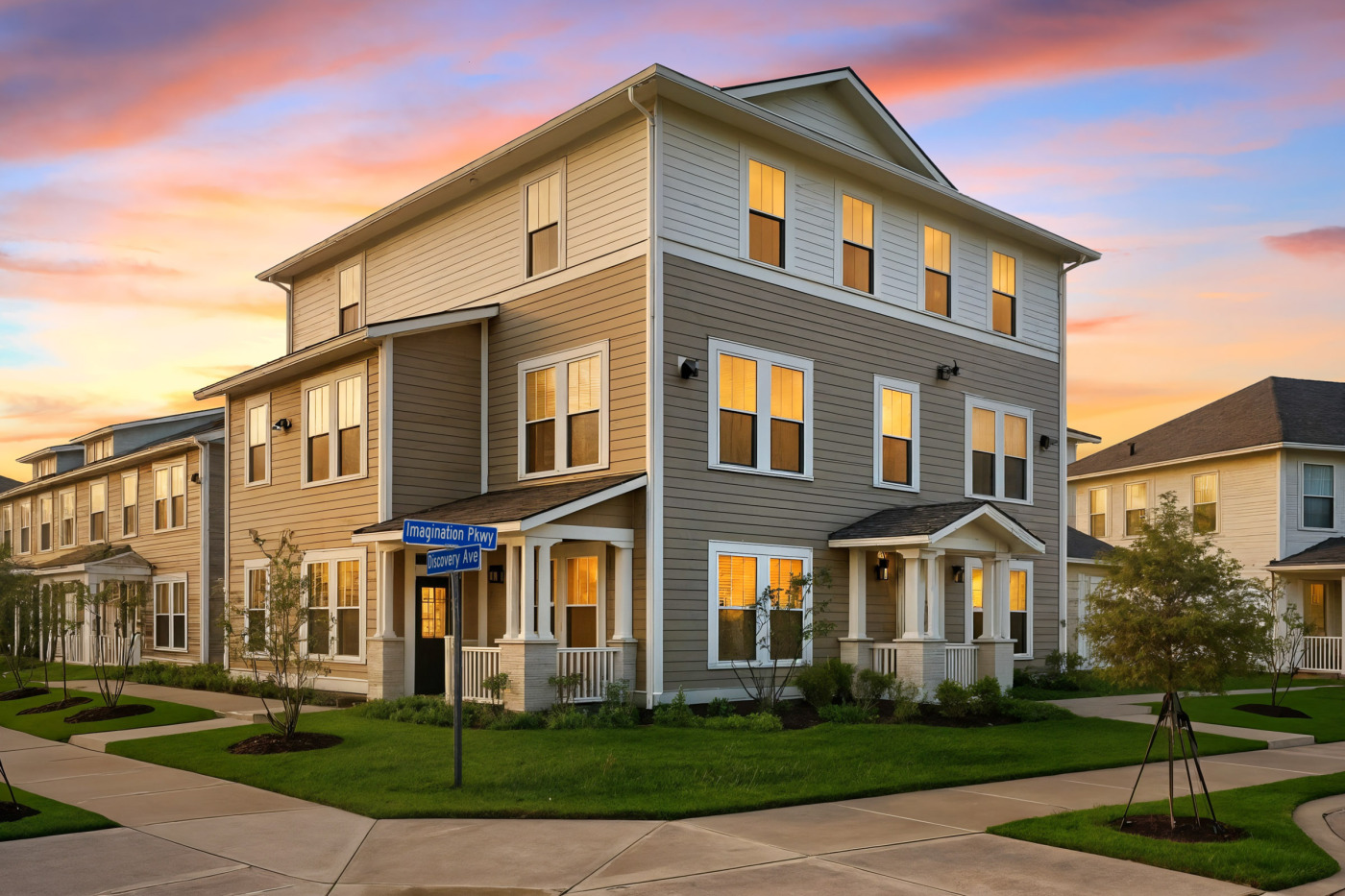 Street-level view of a modern, three-story corner townhome at the intersection of Imagination Parkway and Discovery Avenue, featuring clean lines, neutral colors, white trim, and well-manicured landscaping.