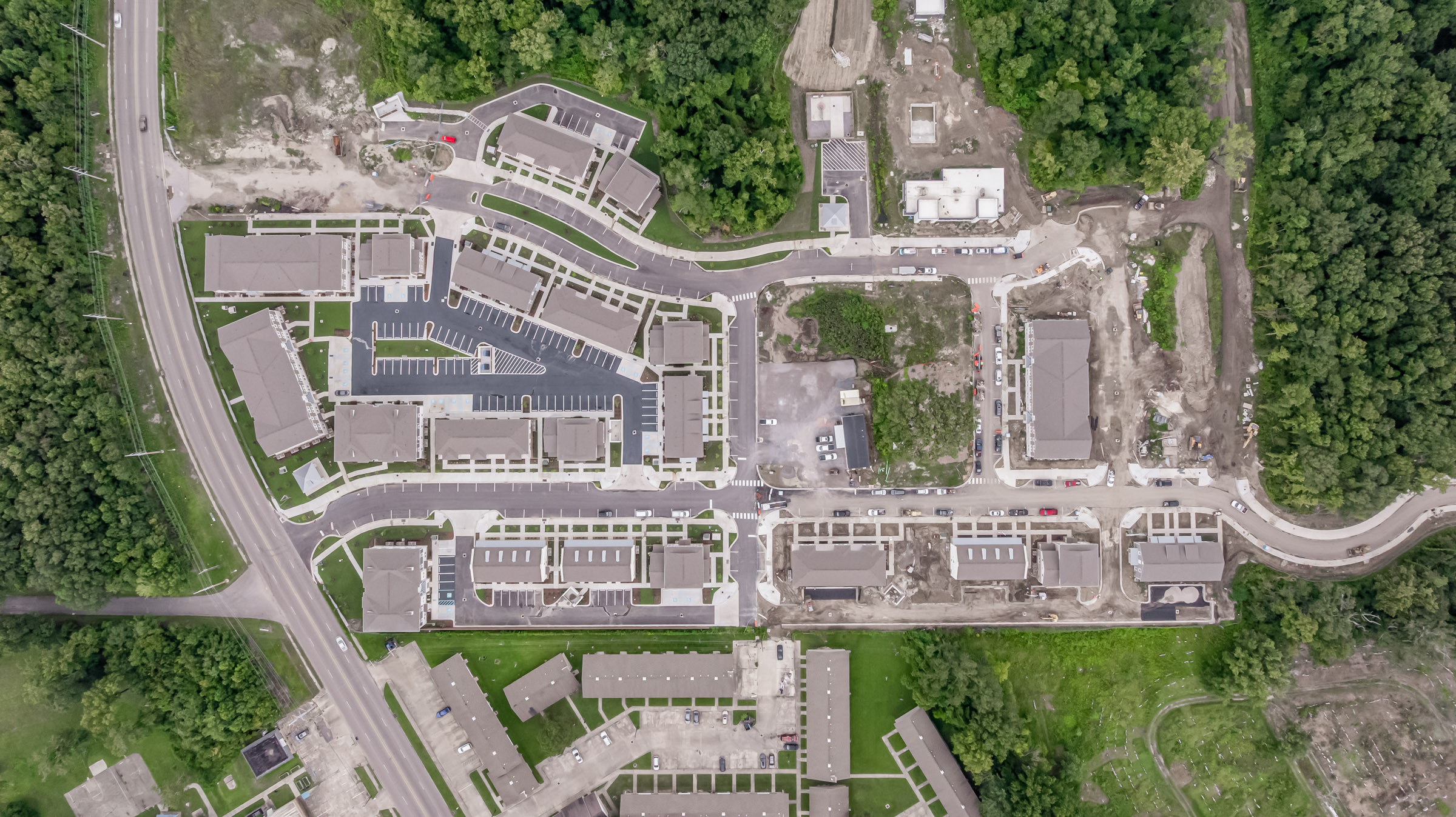 Aerial view of a nearly completed apartment complex featuring multi-story buildings, newly paved roads, parking areas, and landscaped walkways.