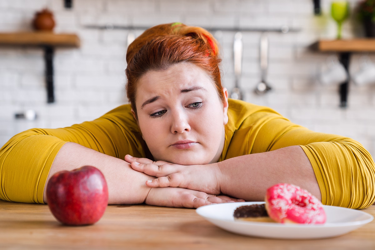 Femeie plinuță care alege între dulciuri și fructe – simbol al dilemei dintre alimentația sănătoasă și tentațiile nesănătoase