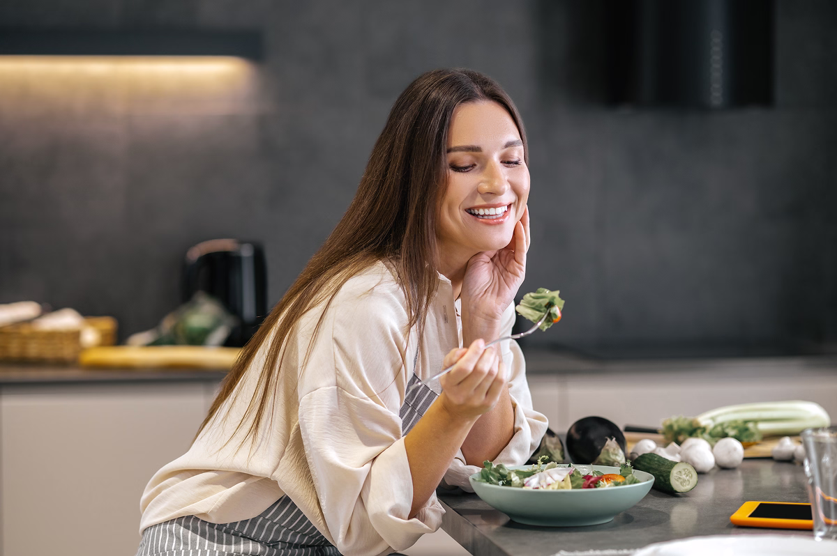 Femeie zâmbitoare care mănâncă prânzul cu poftă – simbol al alimentației corecte, gustoase și echilibrate în procesul de slăbire