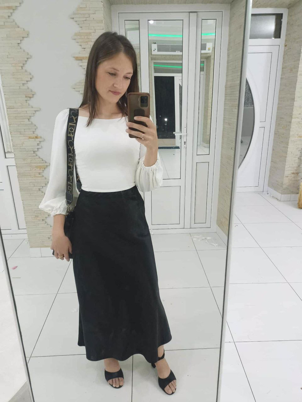 Femeie făcând un selfie în oglindă, purtând o bluză albă și o fustă lungă neagră.
