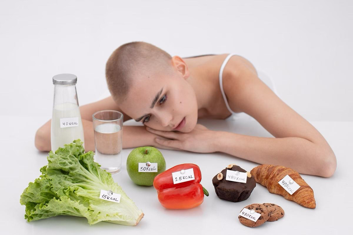 Femeie tânără cu păr scurt privește gânditoare mâncarea etichetată cu calorii, exprimând anxietate legată de alimentație.
