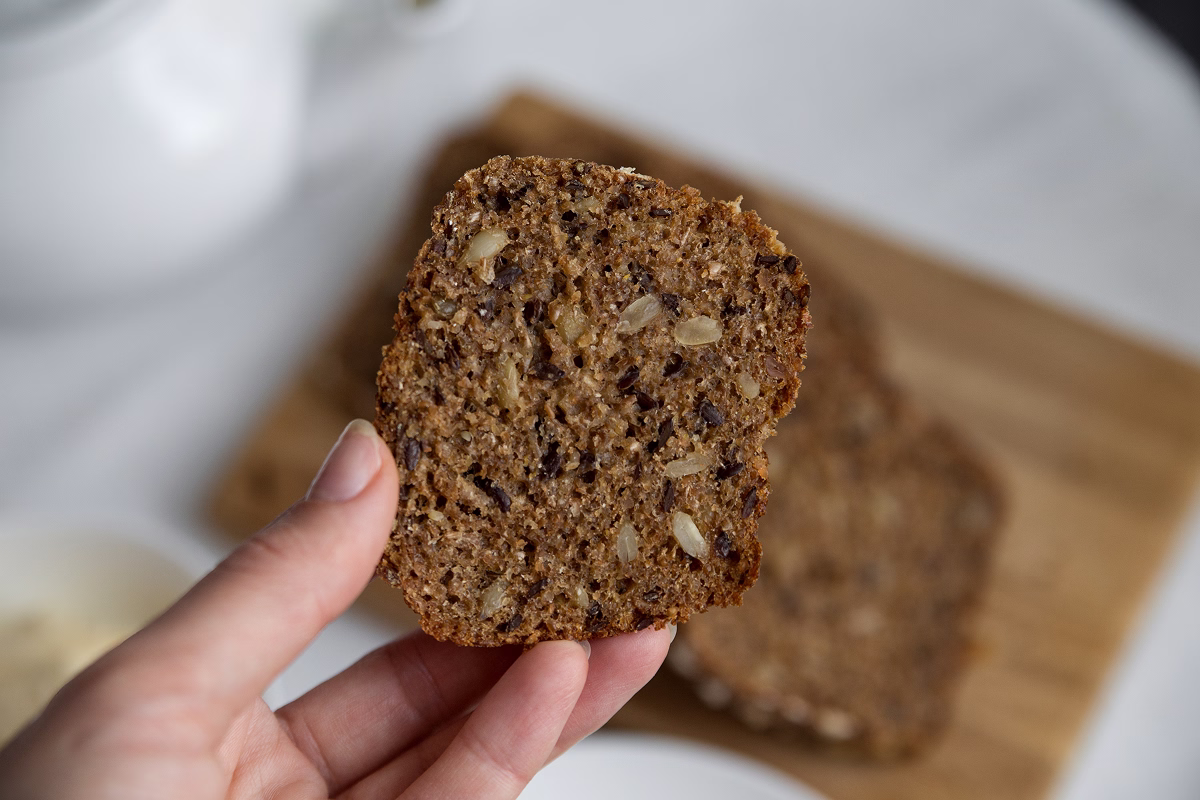 Крупным планом человек держит в руке ломтик цельнозернового хлеба с семечками.