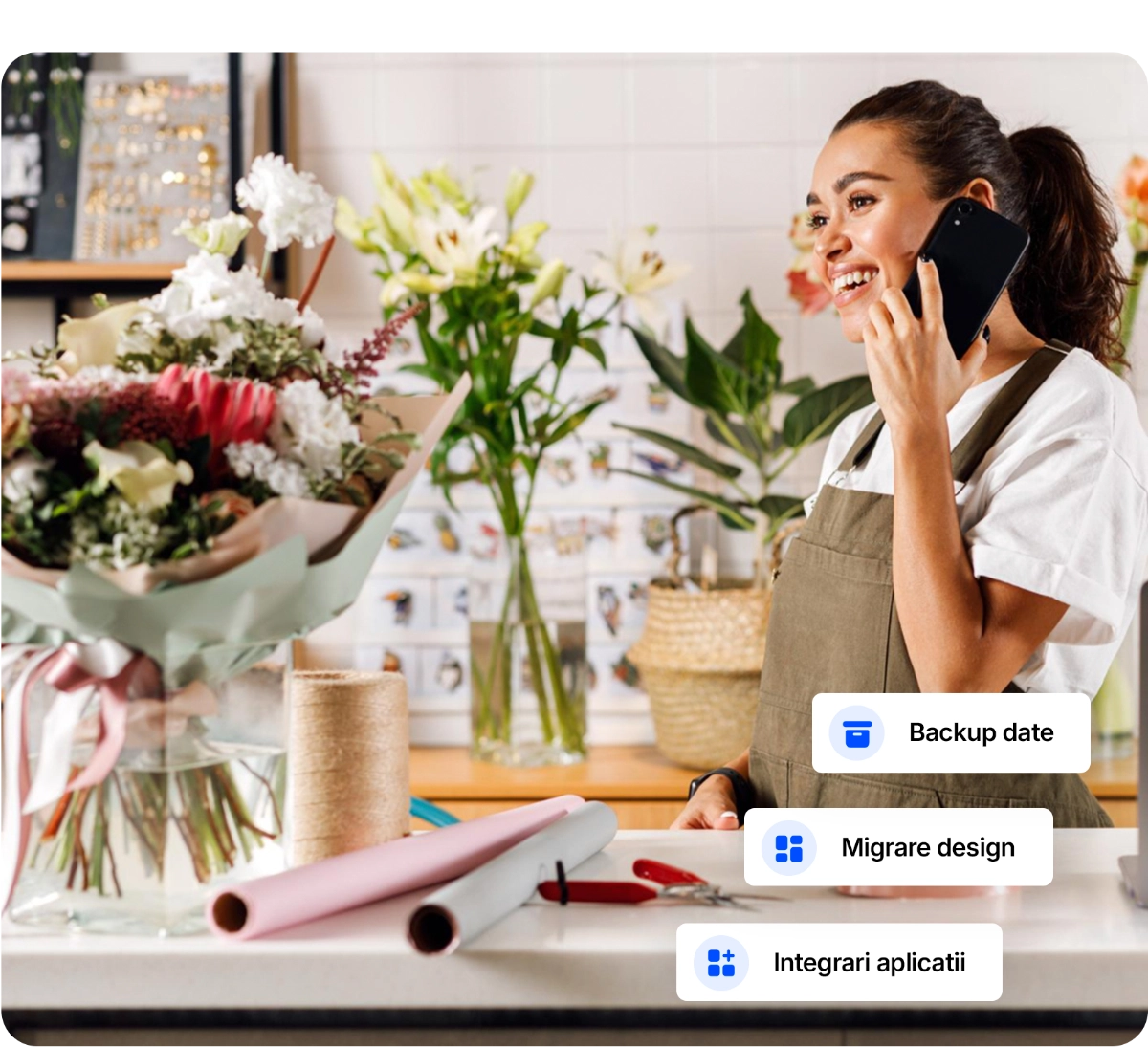 Florareasa zambitoare vorbind la telefon, intr-un atelier de flori, cu un buchet pe masa si optiuni digitale precum backup date, migrare design si integrari aplicatii.