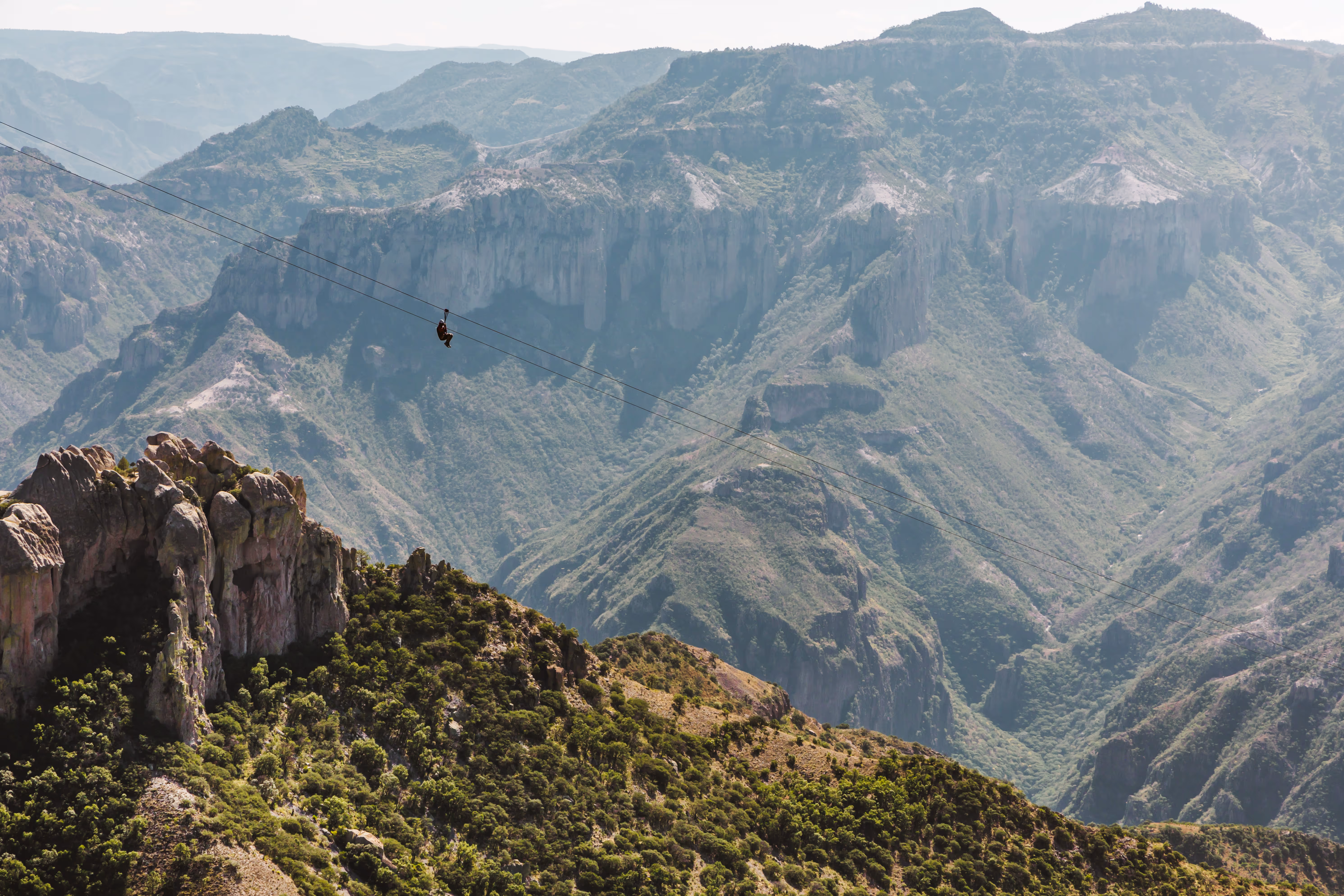 Una persona cruzando montañas en una tirolesa.