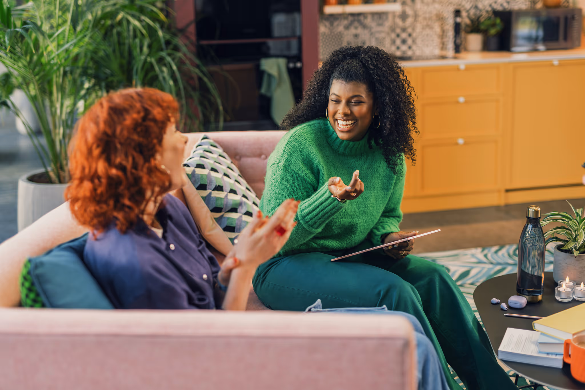 Two woman talking on a couch with a tablet