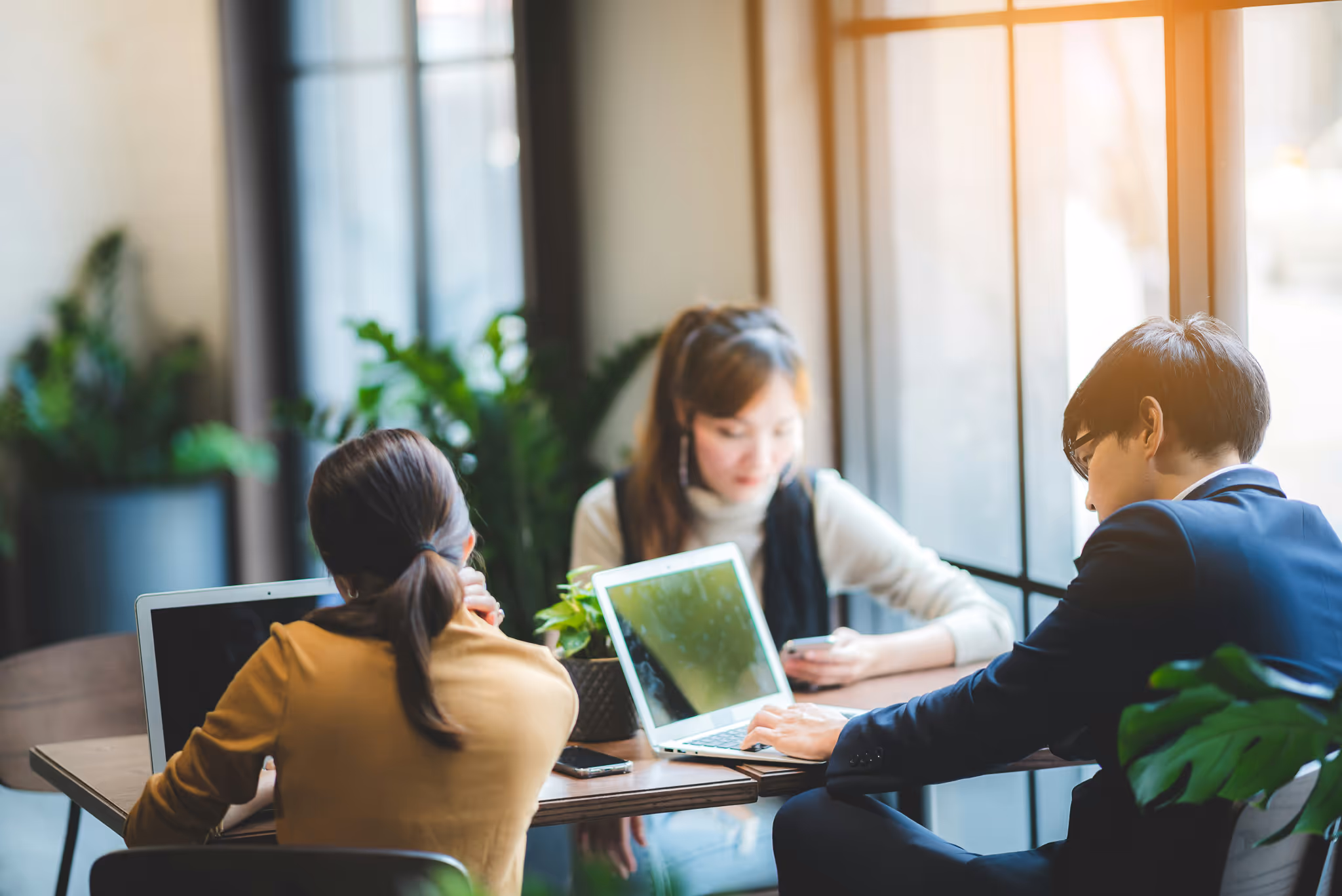 Three people work together on their computers at a table