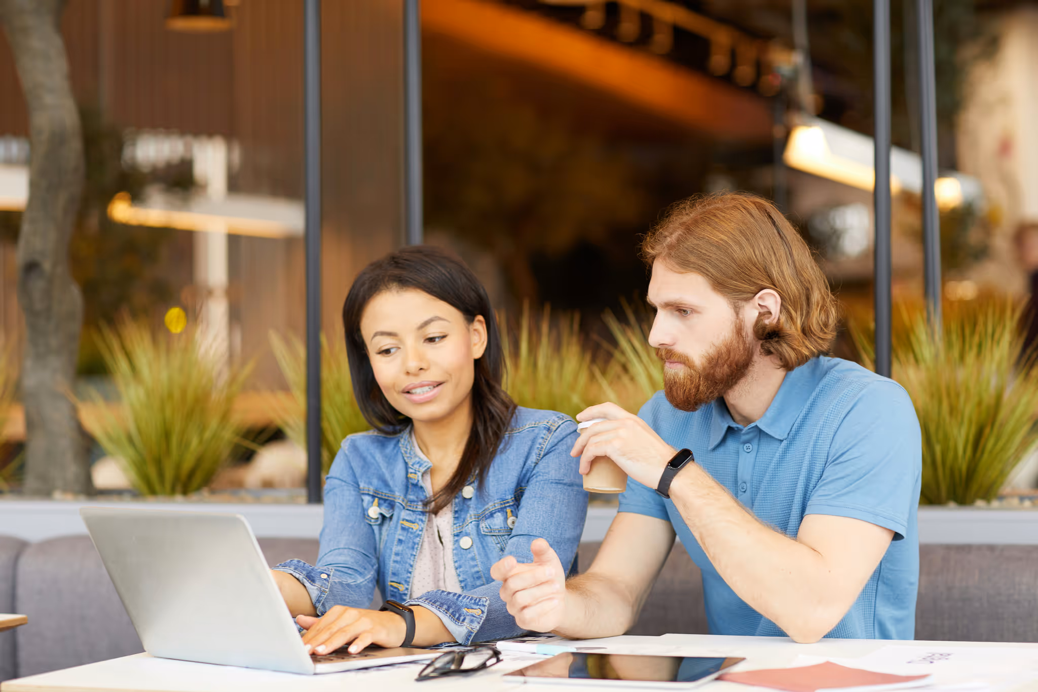 Two people work together and talk at a table with their computer