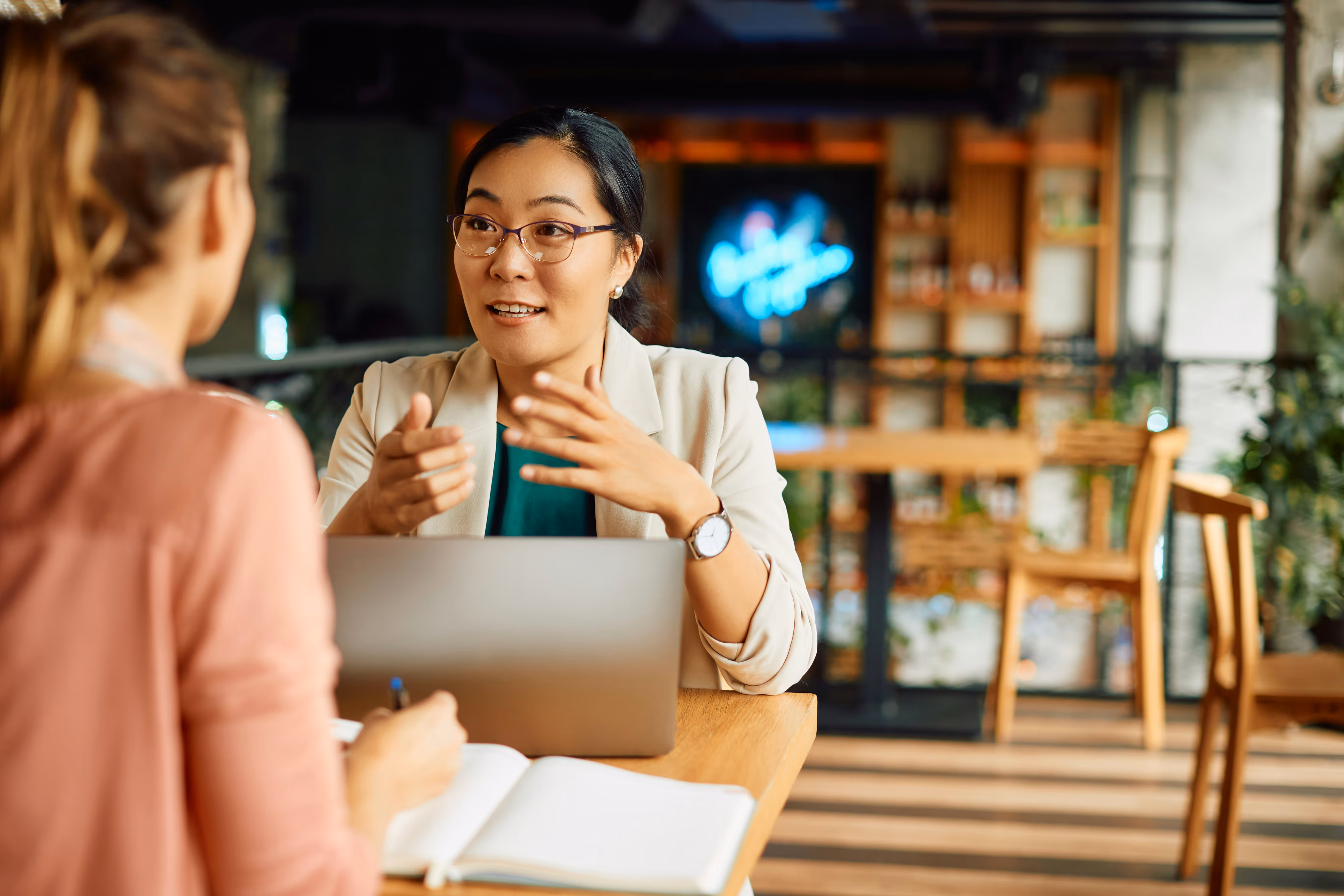 Two business woman talking together at a coffee shop over a computer