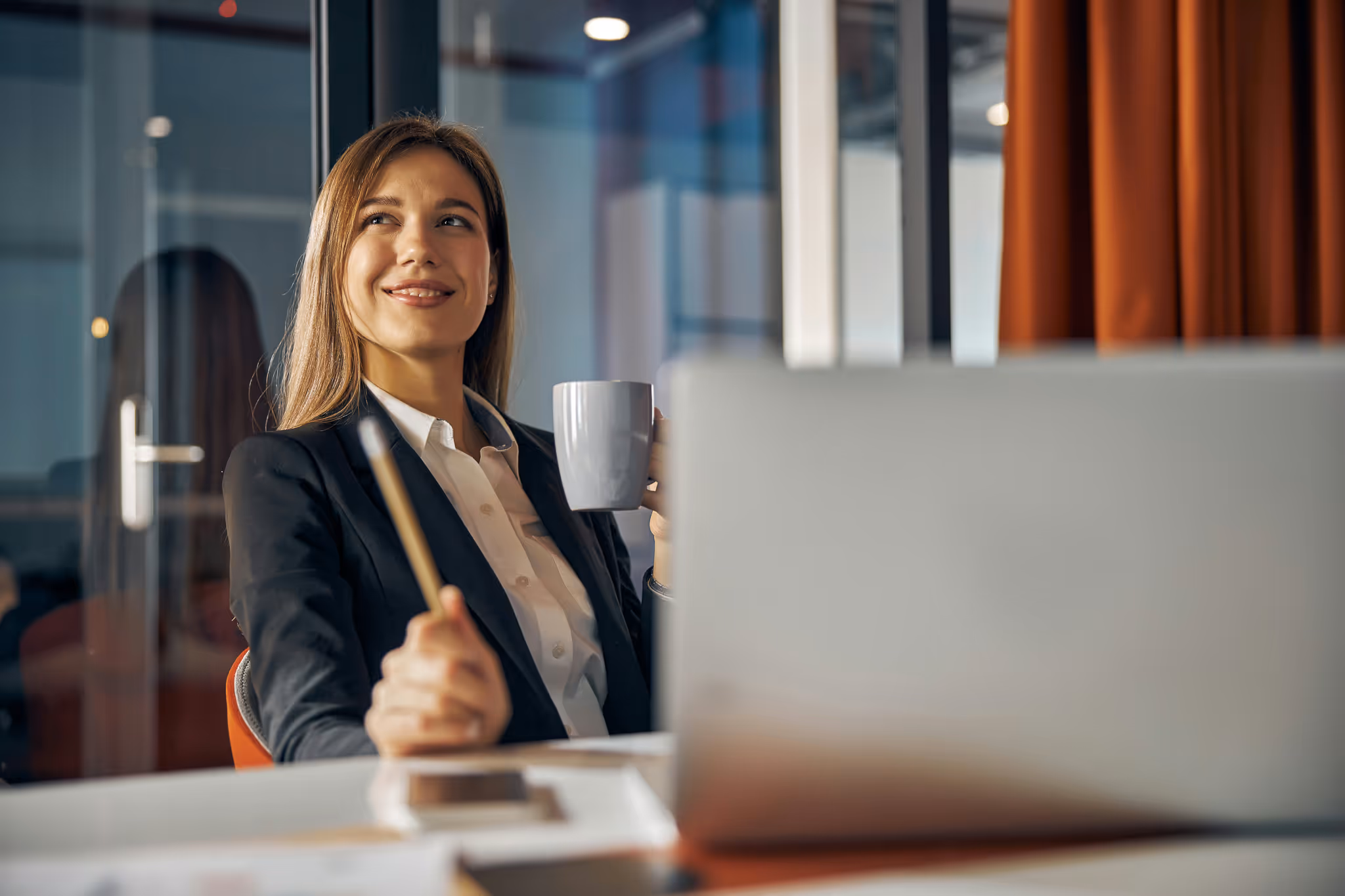 Woman drinking out of a mug while sitting at a desk in front of her computer.