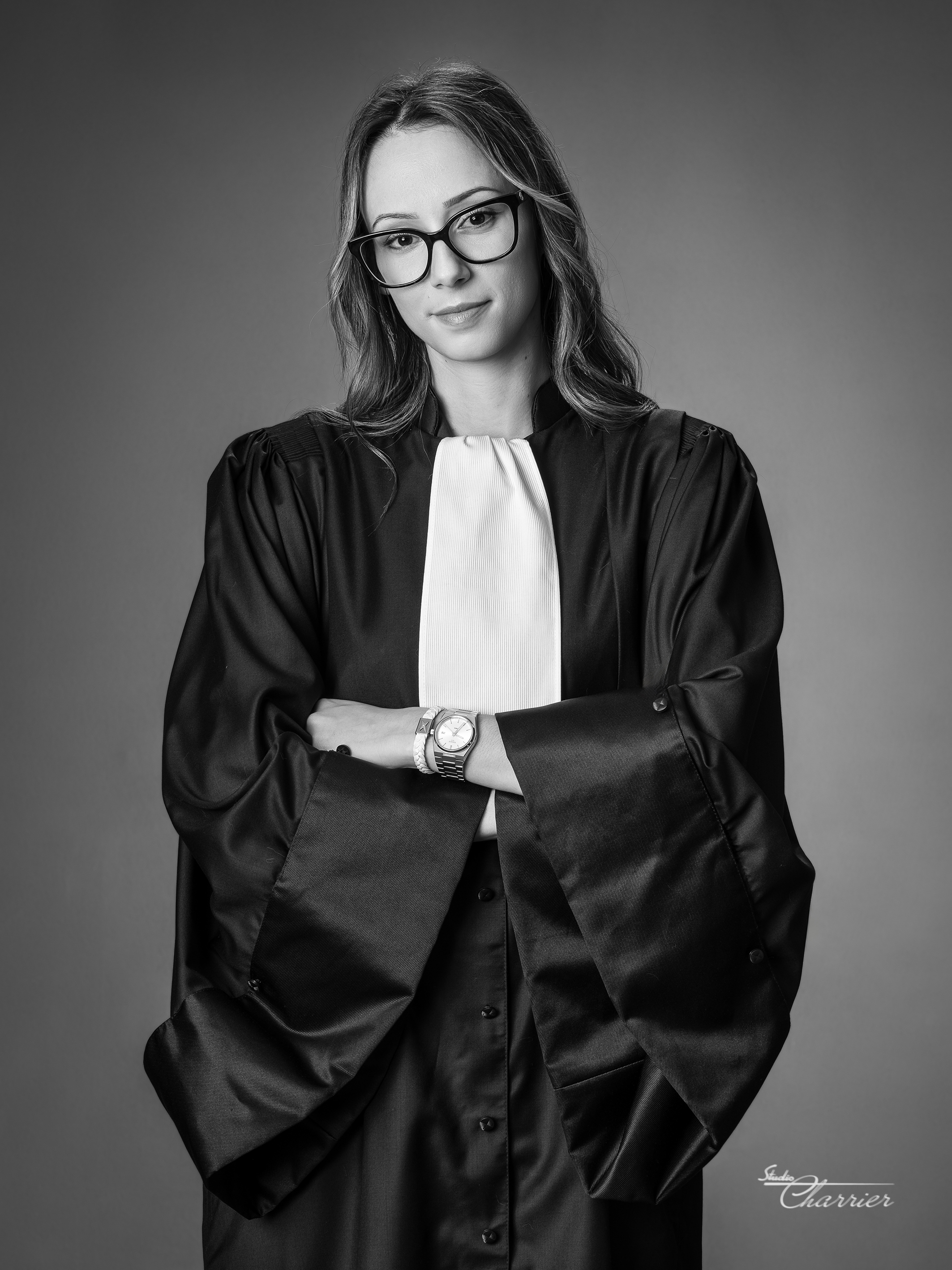 Portrait of a woman wearing glasses and a lawyer's robe with arms crossed, against a plain background.
