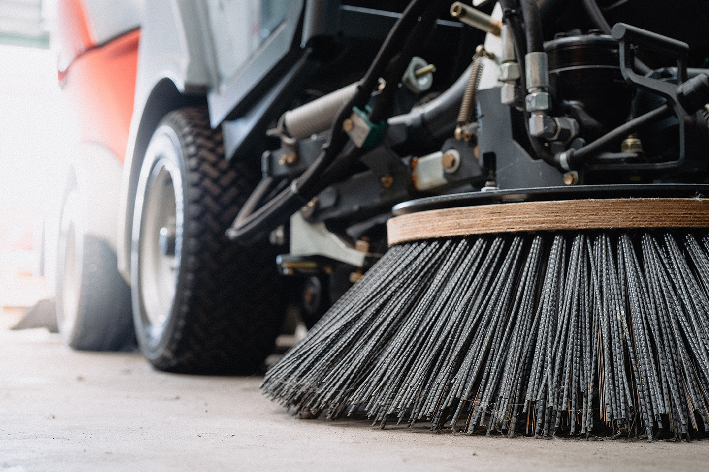 A close-up view of a large street sweeper machine, with the machine's wheels visible in the blurred background. 
