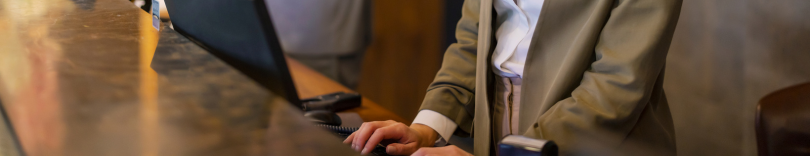 Person in a beige blazer using a desktop computer at a wooden counter or desk.