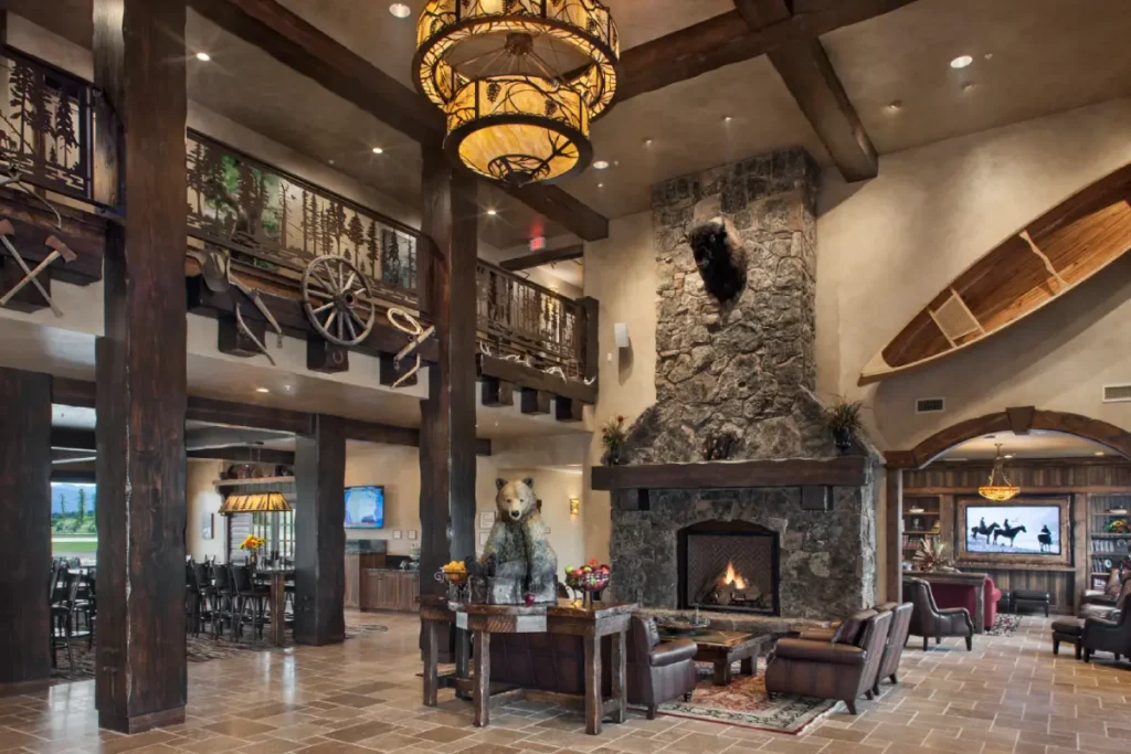 Rustic lodge interior with stone fireplace, mounted bison head, wooden canoe on wall, and cozy leather seating area.