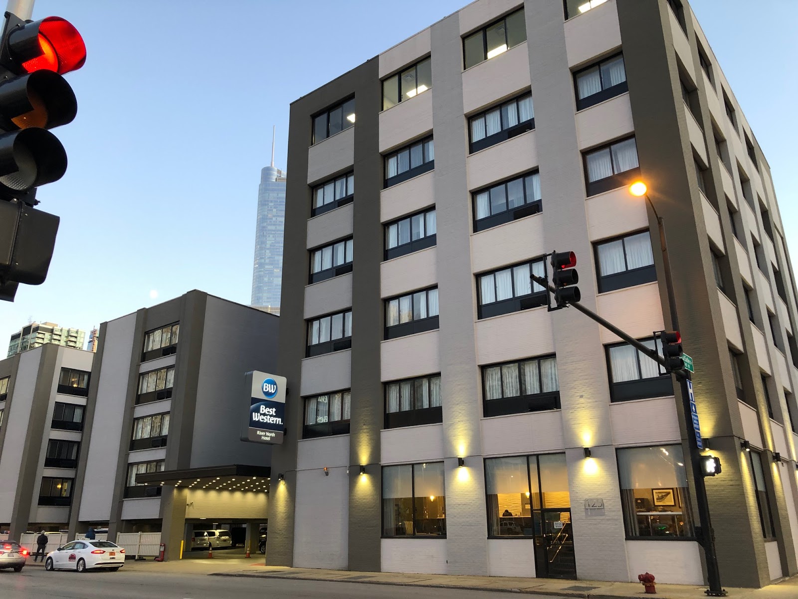 Exterior of the Best Western River North Hotel building at dusk with lit windows and traffic lights showing red.